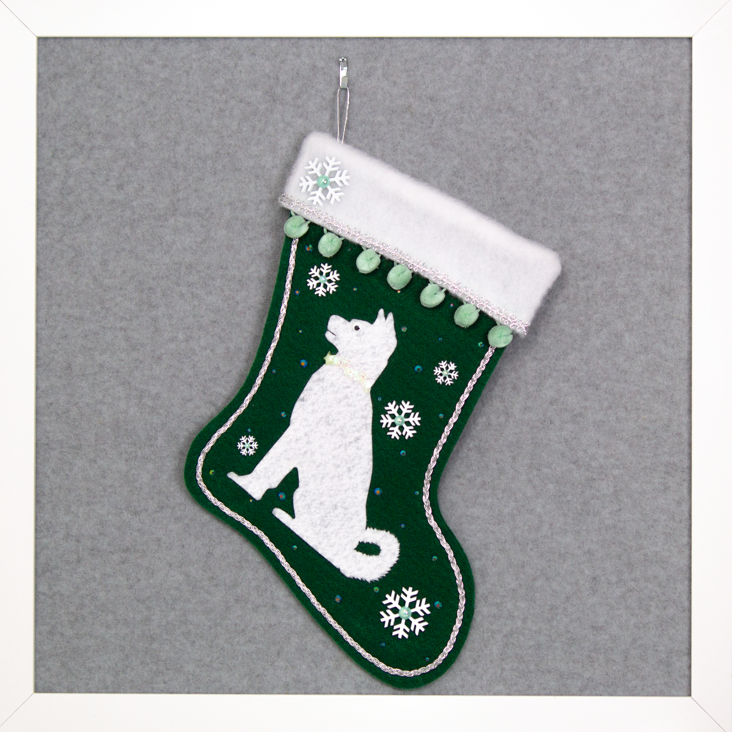 Akita dog in white felt Christmas stocking on  dark green felt with snowflakes, minty green pom poms and decorations in silver and mint green. (Front of stocking)