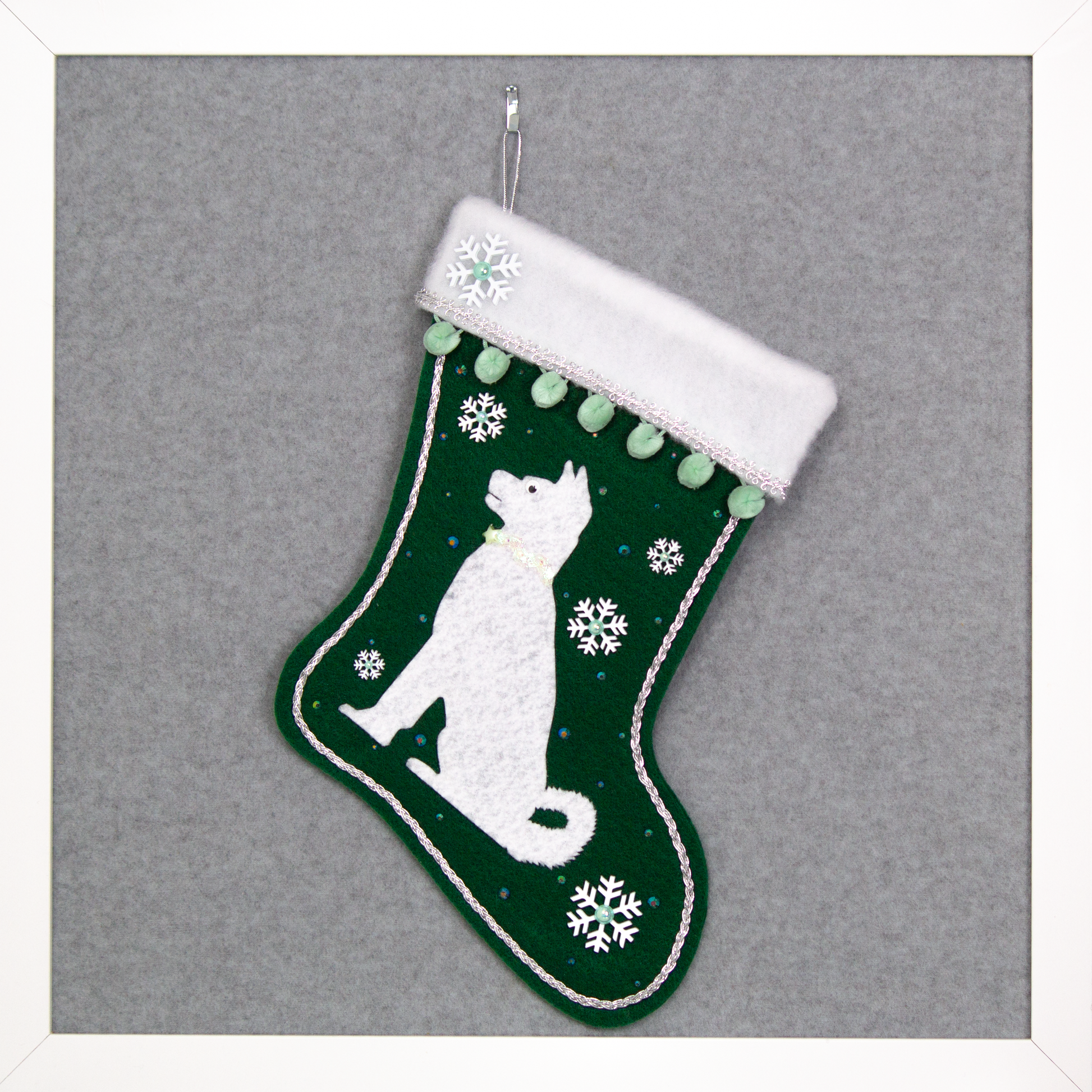 Akita dog in white felt Christmas stocking on  dark green felt with snowflakes, minty green pom poms and decorations in silver and mint green. (Front of stocking)