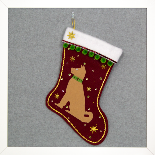 Akita dog in tan felt Christmas stocking on ruby red felt with gold stars, green pom poms and decorations in red, green and gold. (Front of stocking)