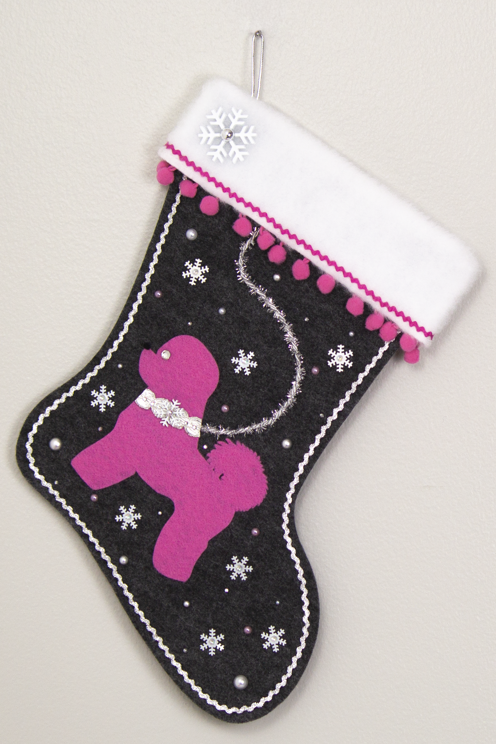 Bichon Frise dog in candy pink felt Christmas stocking on charcoal gray felt with pom poms, tinsel, snowflake sequins and decorations in pink and silver. (Front of stocking)