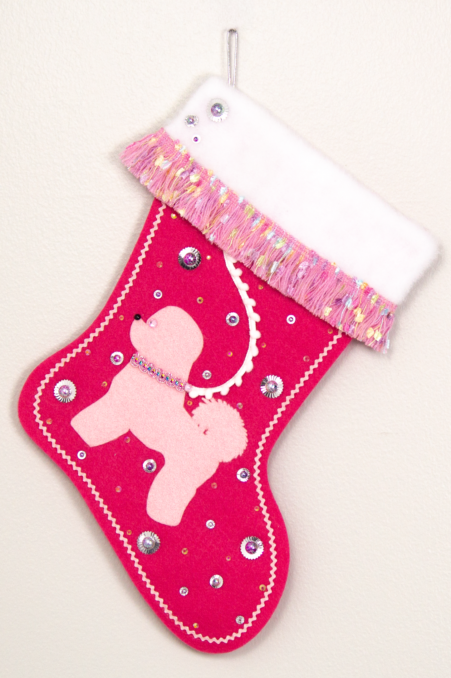 Bichon Frise dog in light pink felt Christmas stocking on candy pink felt with fringe, sequins, mini pom poms and decorations in multicolor and silver. (Front of stocking)