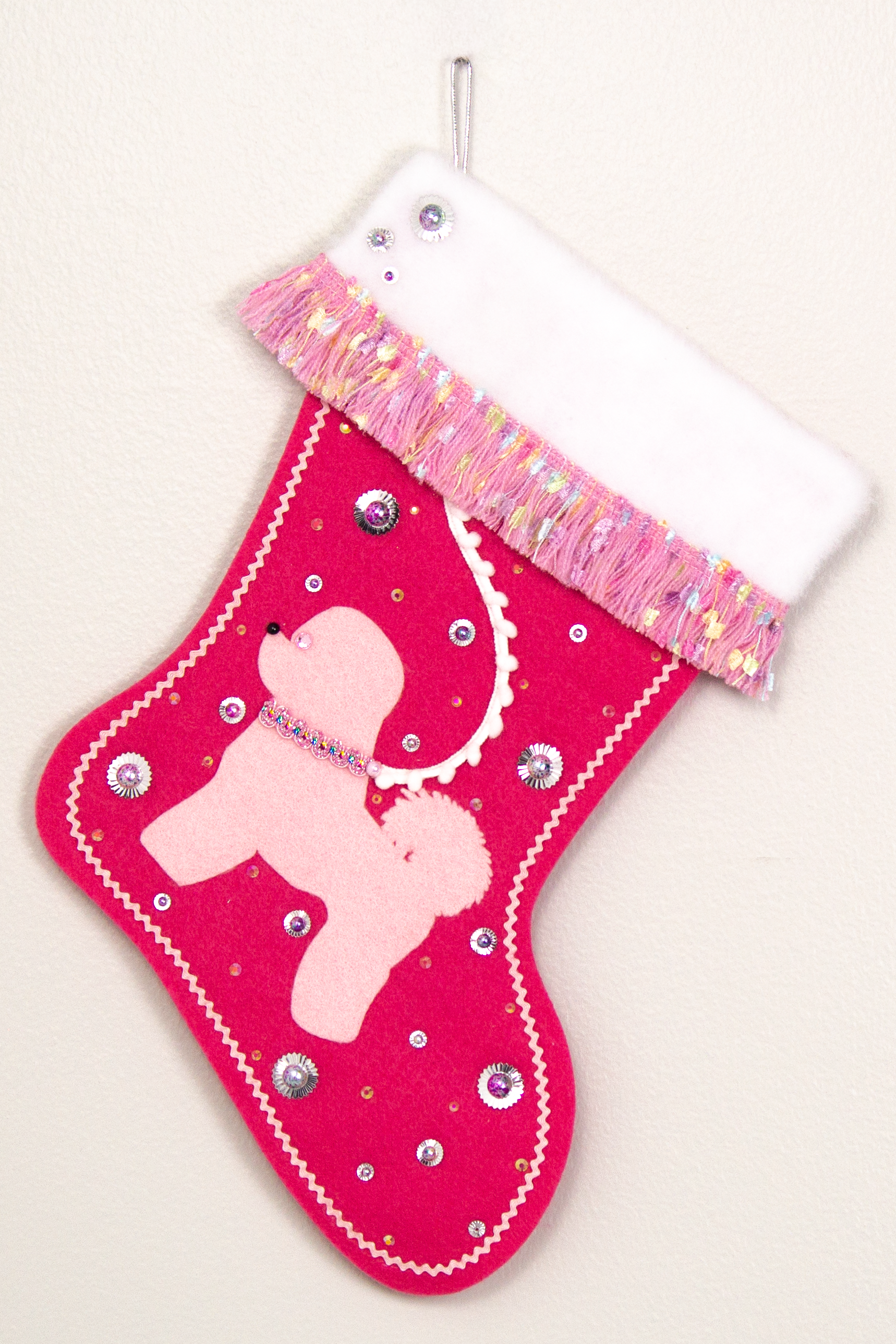 Bichon Frise dog in light pink felt Christmas stocking on candy pink felt with fringe, sequins, mini pom poms and decorations in multicolor and silver. (Front of stocking)