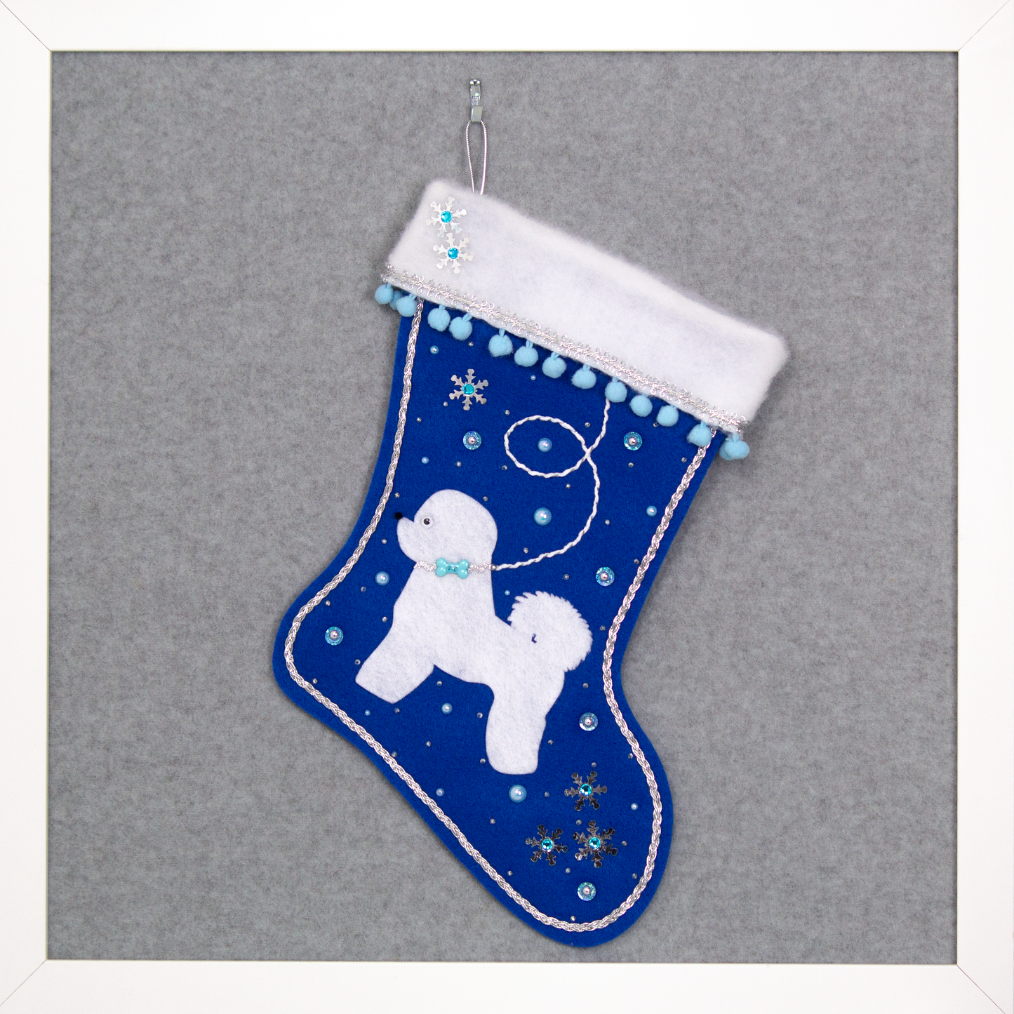 Bichon Frise dog in white felt Christmas stocking on royal blue felt with sequin stars, pom poms and decorations in light blue, white and silver. (Front of stocking)