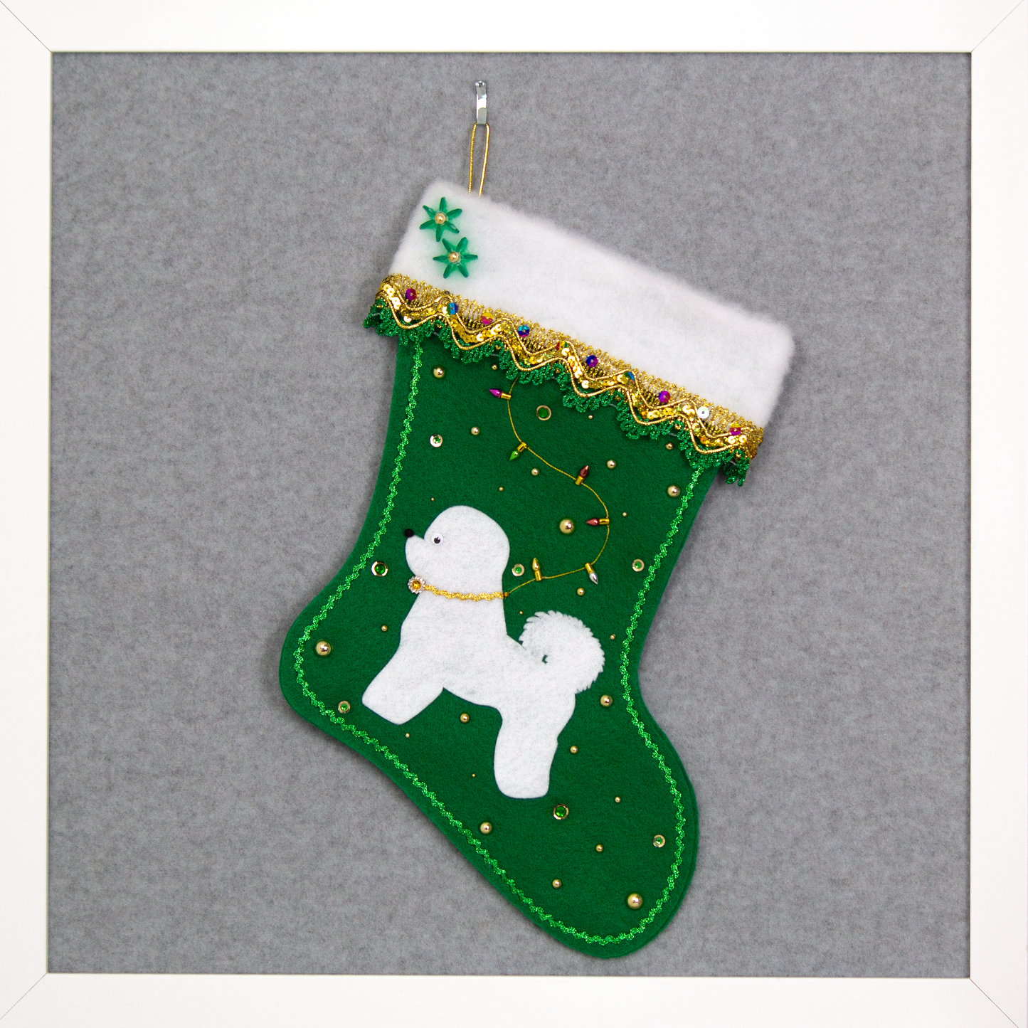 Bichon Frise dog in white felt Christmas stocking on holiday green felt with fancy gold trim, a string of "lights" and decorations in green and gold. (Front of stocking)