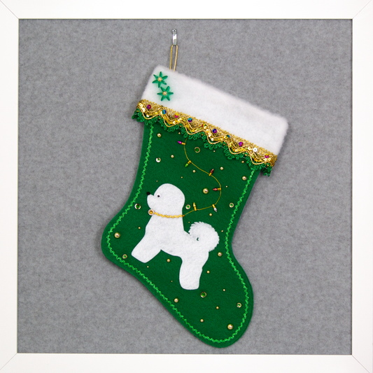 Bichon Frise dog in white felt Christmas stocking on holiday green felt with fancy gold trim, a string of "lights" and decorations in green and gold. (Front of stocking)