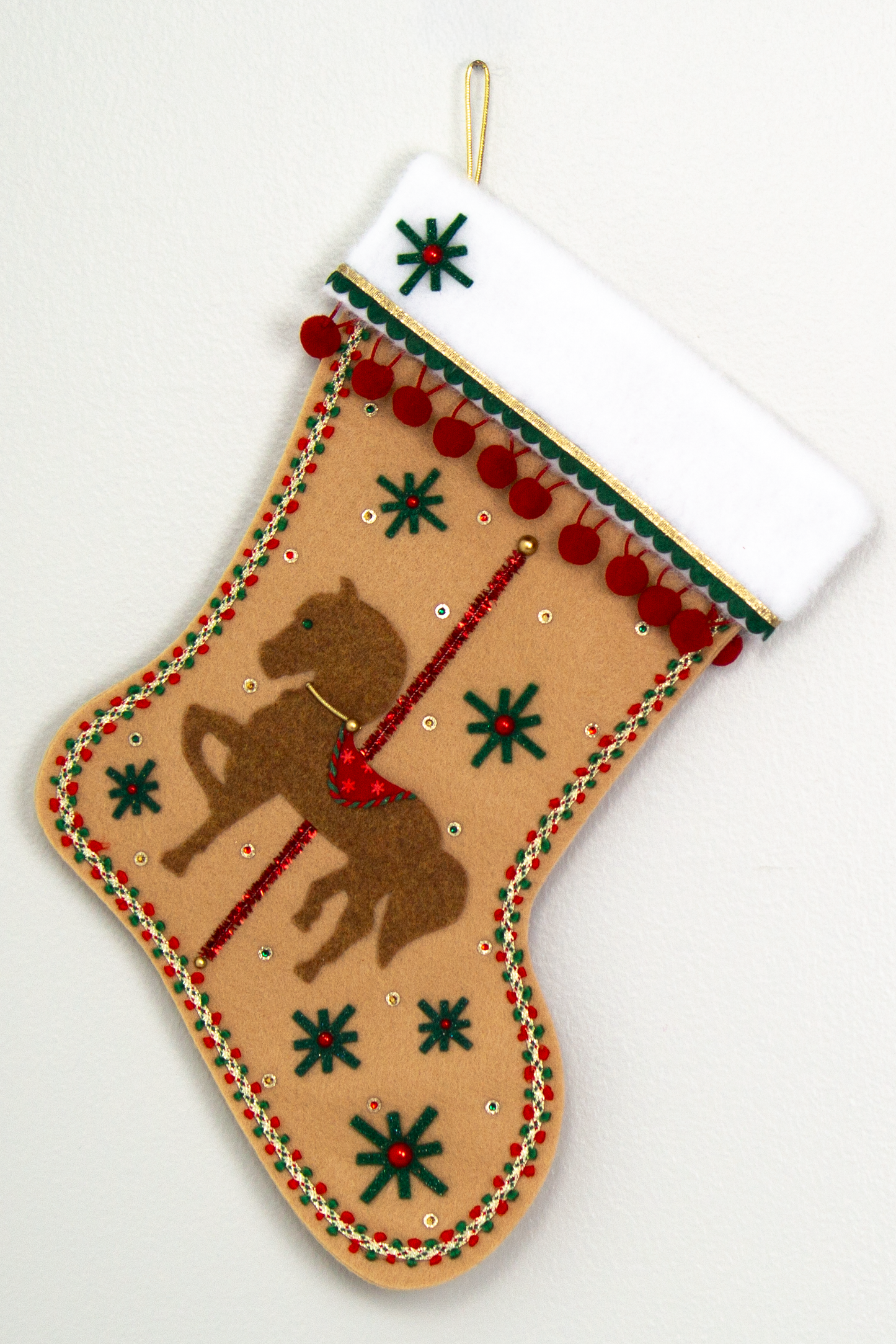 Copper felt horse on tan felt handmade Christmas stocking with pom poms, felt starbursts, tinsel pipe cleaner pole and decorated in red, dark green & gold. (front of Carousel Horse stocking)
