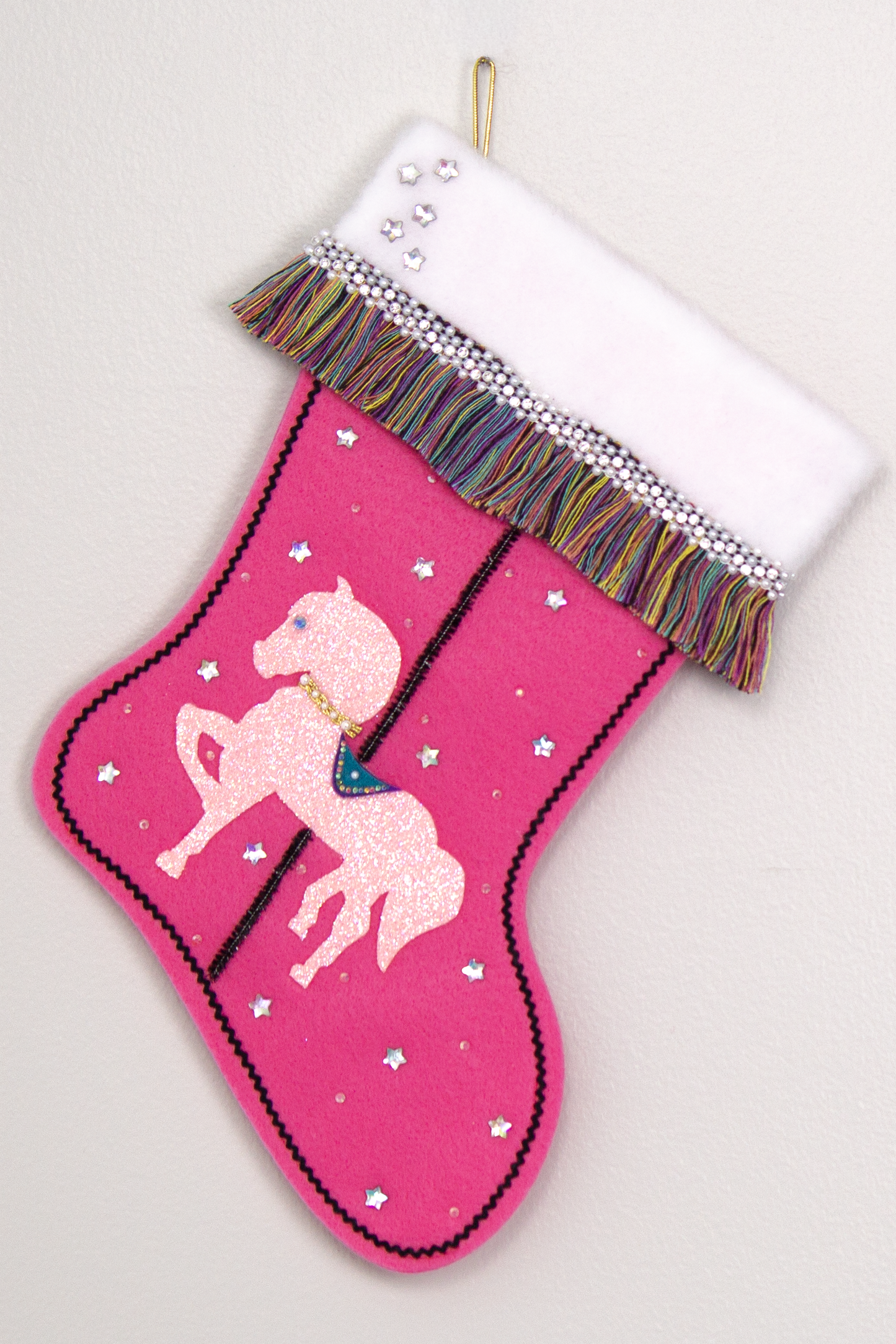 Light pink glittered horse on candy pink felt handmade Christmas stocking with multicolor fringe, star rhinestones, tinsel pipe cleaner pole and decorations in white, clear, holographic, turquoise, purple, black & gold. (front of Carousel Horse stocking)