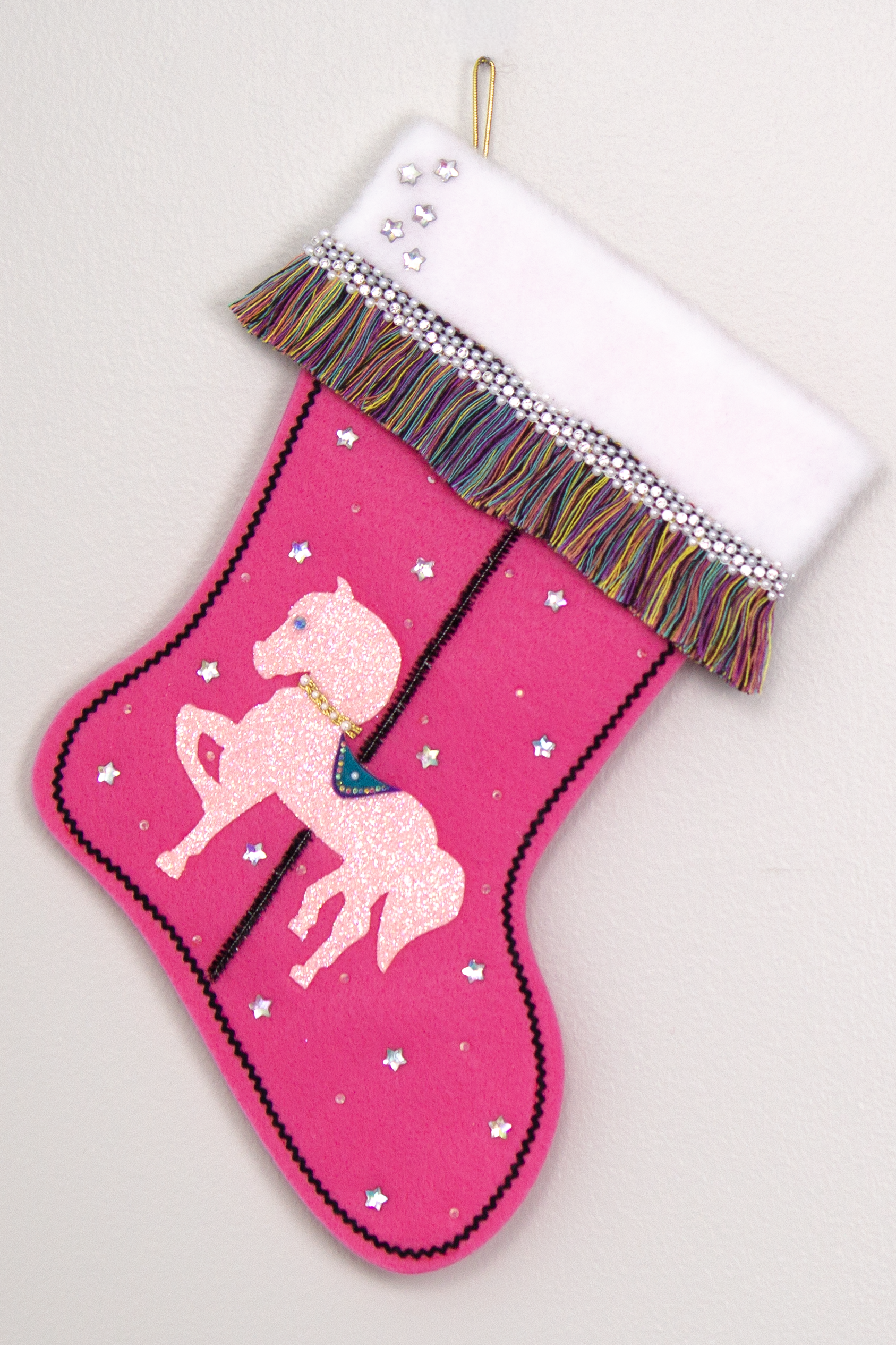 Light pink glittered horse on candy pink felt handmade Christmas stocking with multicolor fringe, star rhinestones, tinsel pipe cleaner pole and decorations in white, clear, holographic, turquoise, purple, black & gold. (front of Carousel Horse stocking)