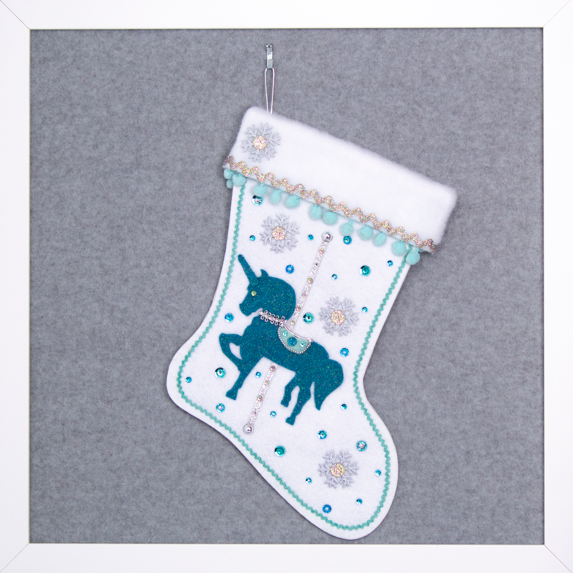 Turquoise felt glittered unicorn on a white glitter felt handmade Christmas stocking with pom poms, snowflake buttons and decorations in aqua, turquoise, white & silver. (front of Carousel Unicorn stocking)