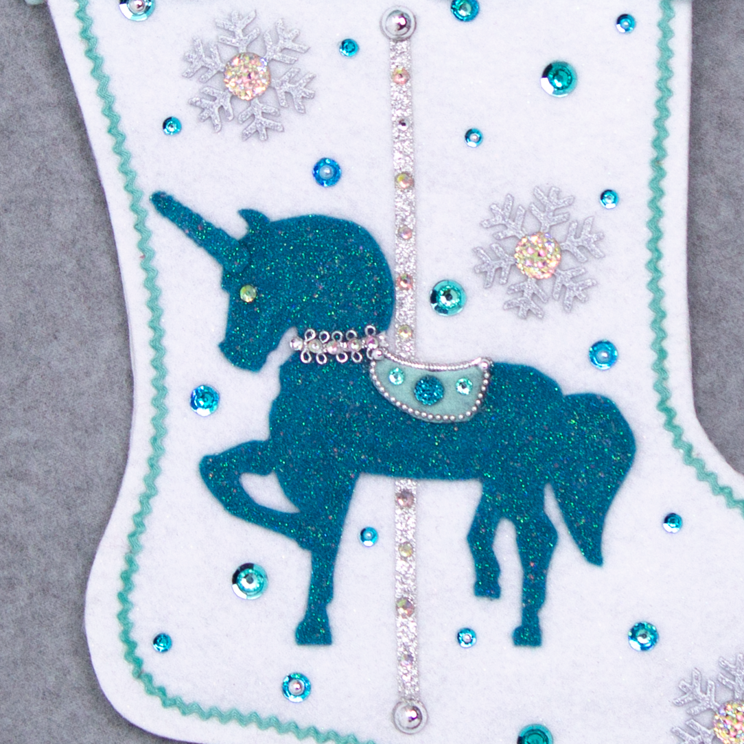 Turquoise felt glittered unicorn on a white glitter felt handmade Christmas stocking with pom poms, snowflake buttons and decorations in aqua, turquoise, white & silver. (front of Carousel Unicorn stocking - close up detail of unicorn)