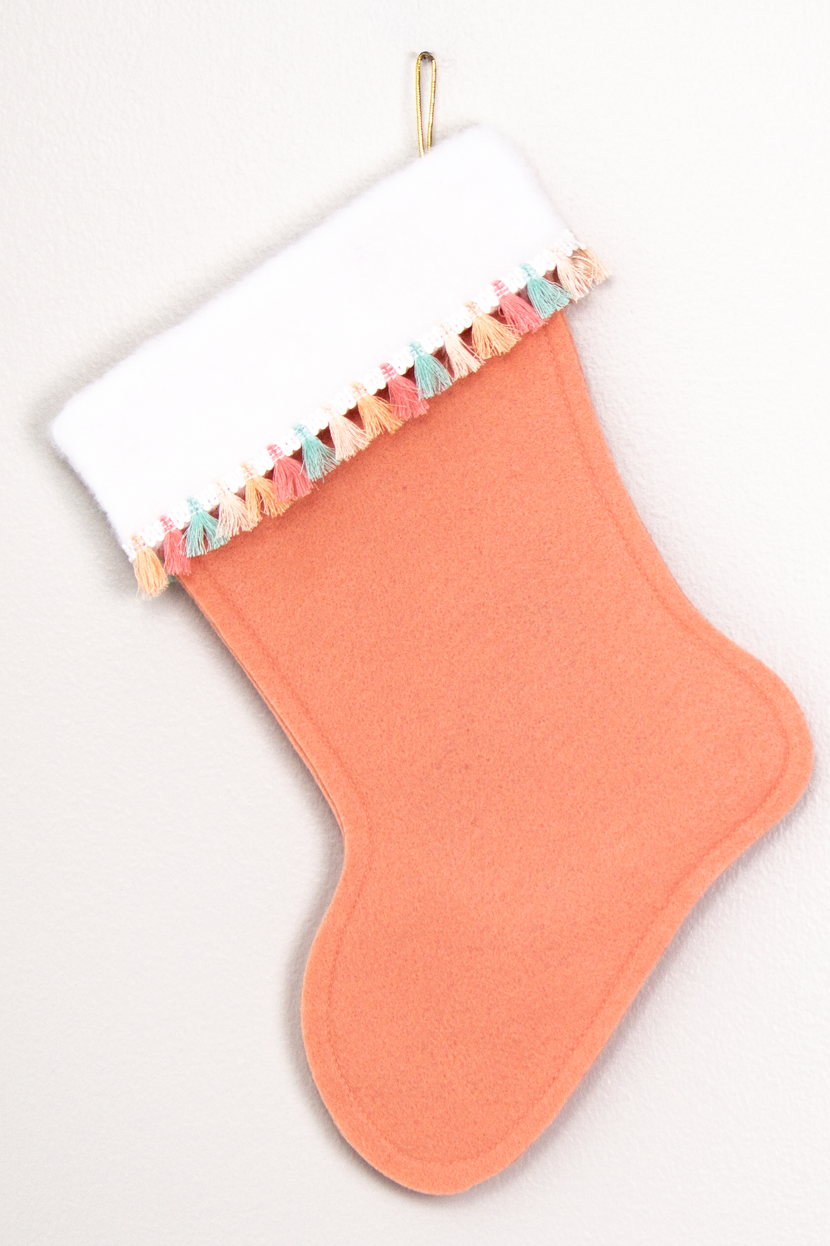 Coral felt handmade Christmas stocking with tassel fringe and decorated in gold  & multicolored pastels. (back of Carousel Unicorn stocking)