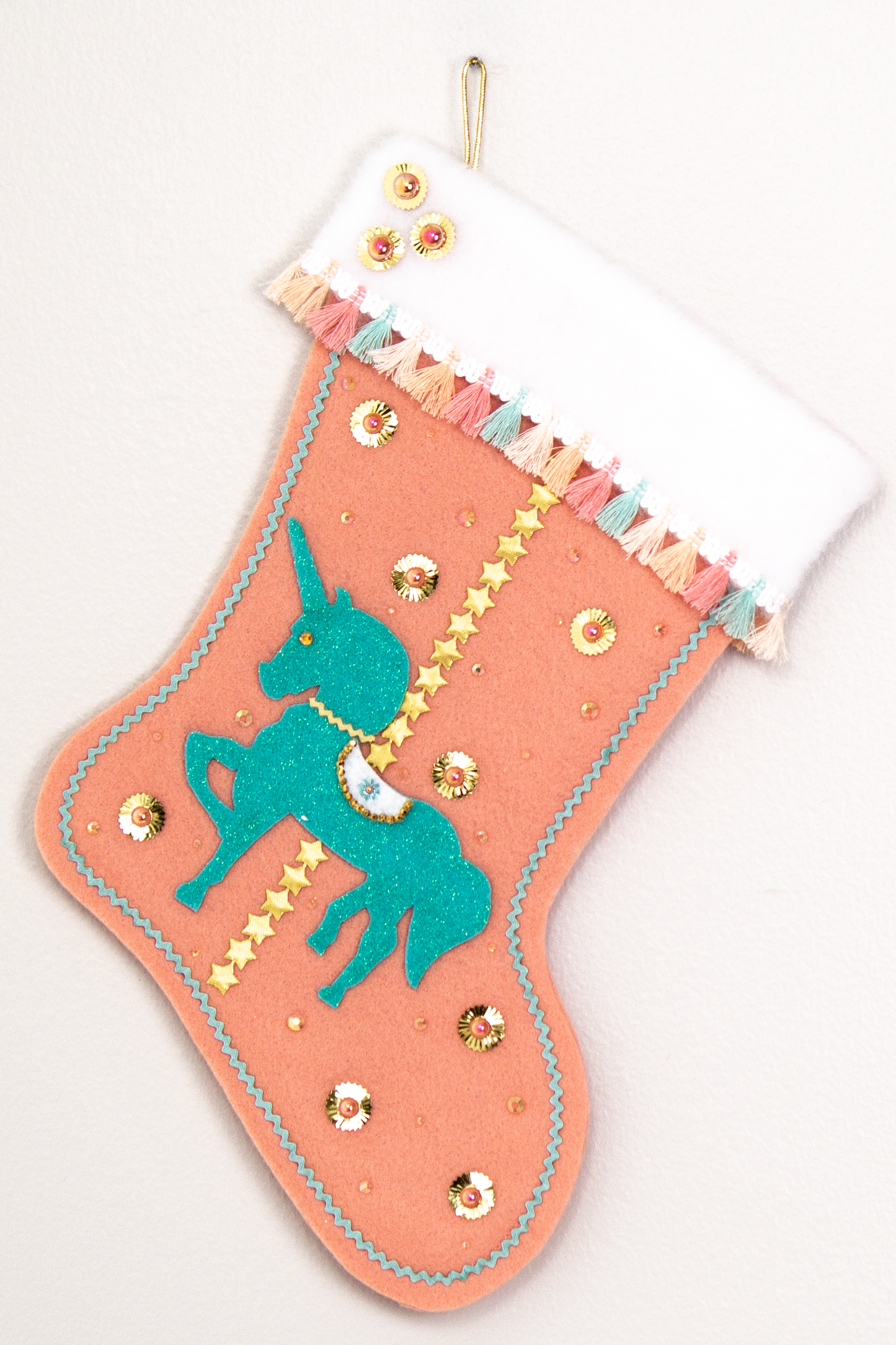 Aqua glittered unicorn on coral felt handmade Christmas stocking with tassel fringe, stars, sunburst sequins and decorated in gold, coral, aqua & multicolored pastels. (front of Carousel Unicorn stocking)