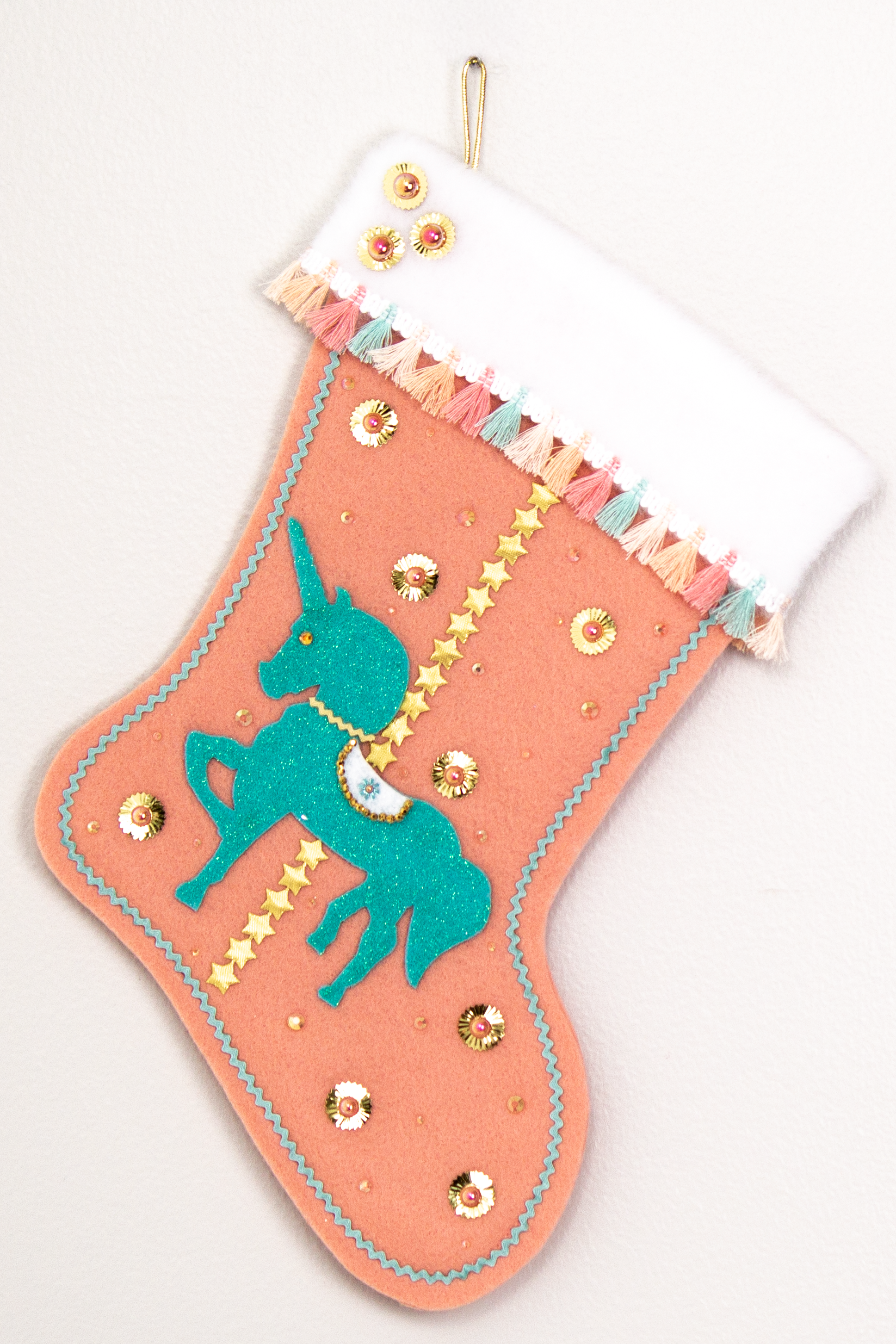 Aqua glittered unicorn on coral felt handmade Christmas stocking with tassel fringe, stars, sunburst sequins and decorated in gold, coral, aqua & multicolored pastels. (front of Carousel Unicorn stocking)