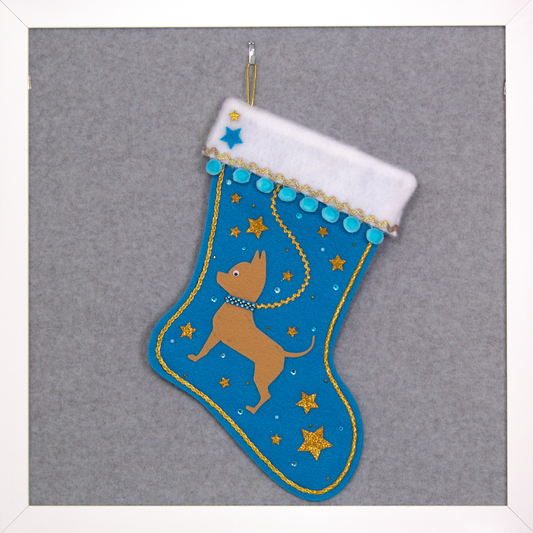Tan short hair Chihuahua dog on peacock blue felt Christmas stocking with pom poms, glitter stars and decorations in blue and gold. (front of stocking)