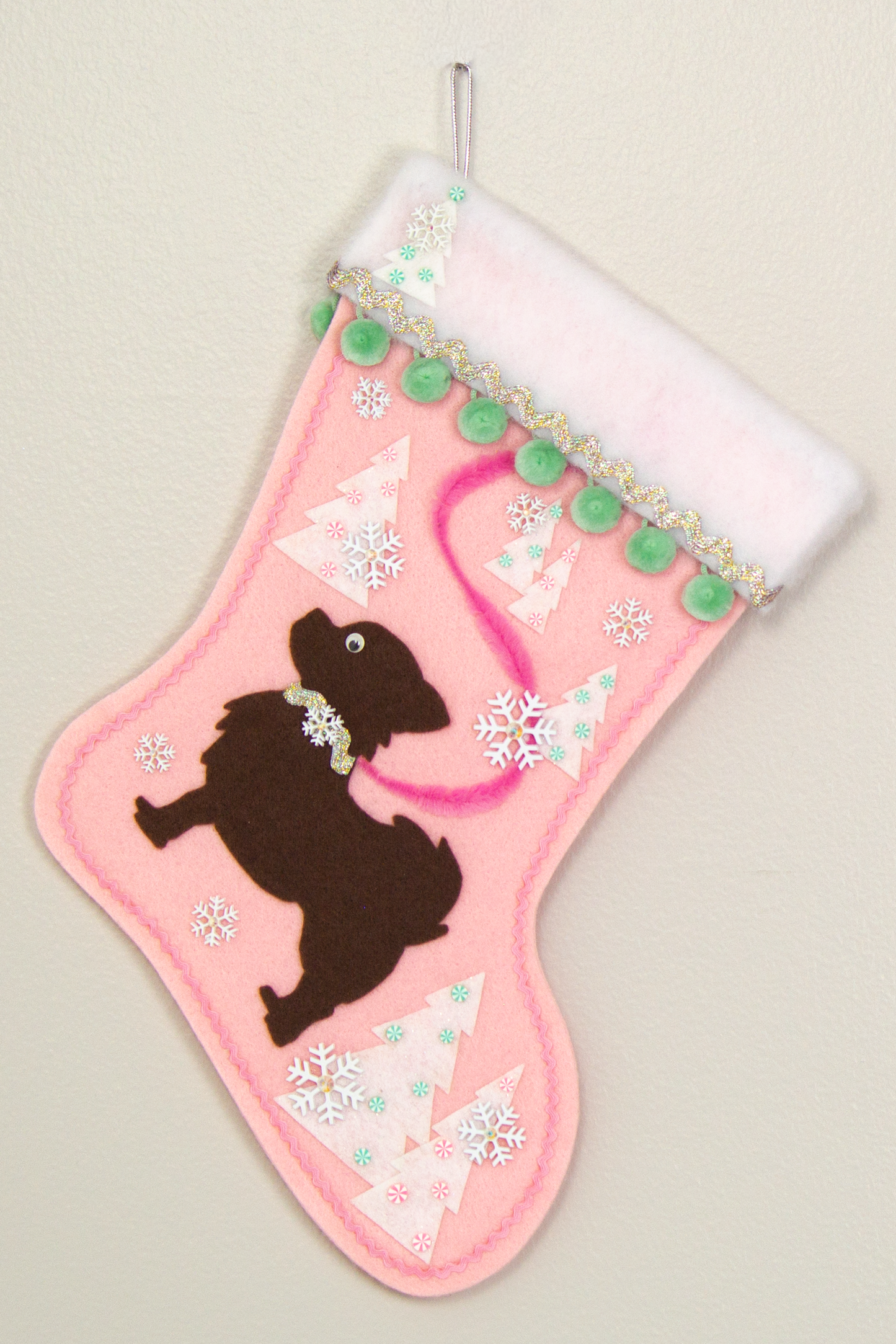 Chocolate brown long hair Chihuahua dog silhouette on a light pink felt Christmas stocking with pom poms, trees, snowflakes and decorations in mint green, pink, white and silver. (front of stocking)