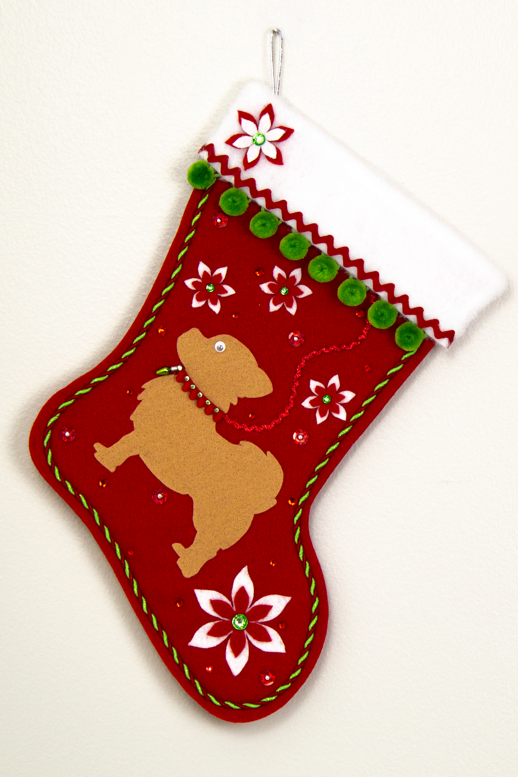 Red glitter Christmas stocking with tan long hair Chihuahua small dog silhouette with pom poms, felt poinsettias and decorations in green, red and silver. (front of stocking)