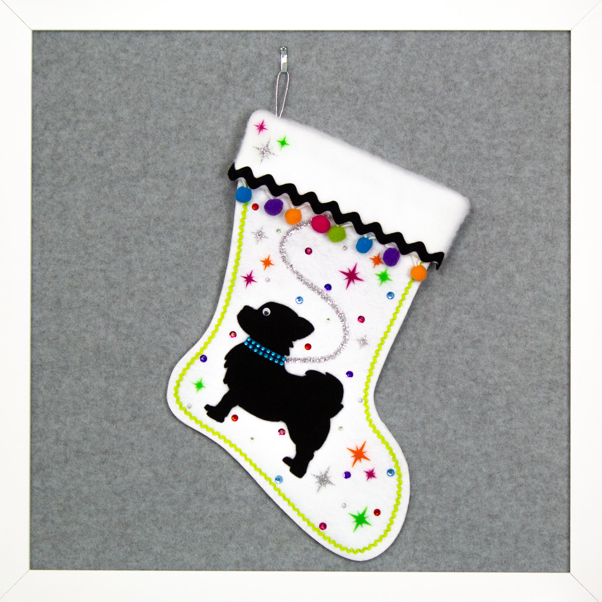 White glitter Christmas stocking with black long hair Chihuahua small dog silhouette with pom poms, starbursts and decorations in black, silver, hot pink, lime green, orange, purple and blue. (front of stocking)