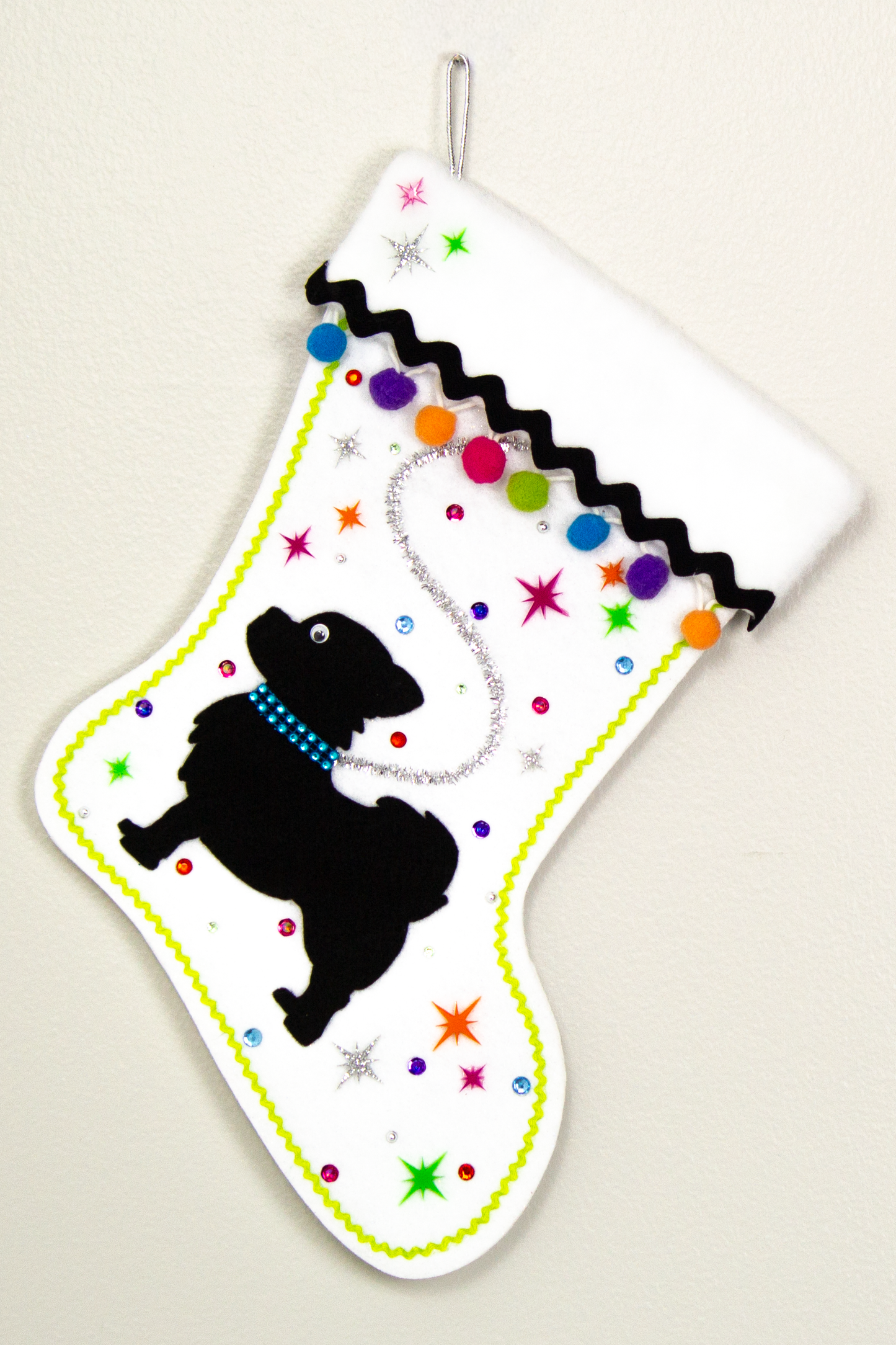 White glitter Christmas stocking with black long hair Chihuahua small dog silhouette with pom poms, starbursts and decorations in black, silver, hot pink, lime green, orange, purple and blue. (front of stocking)