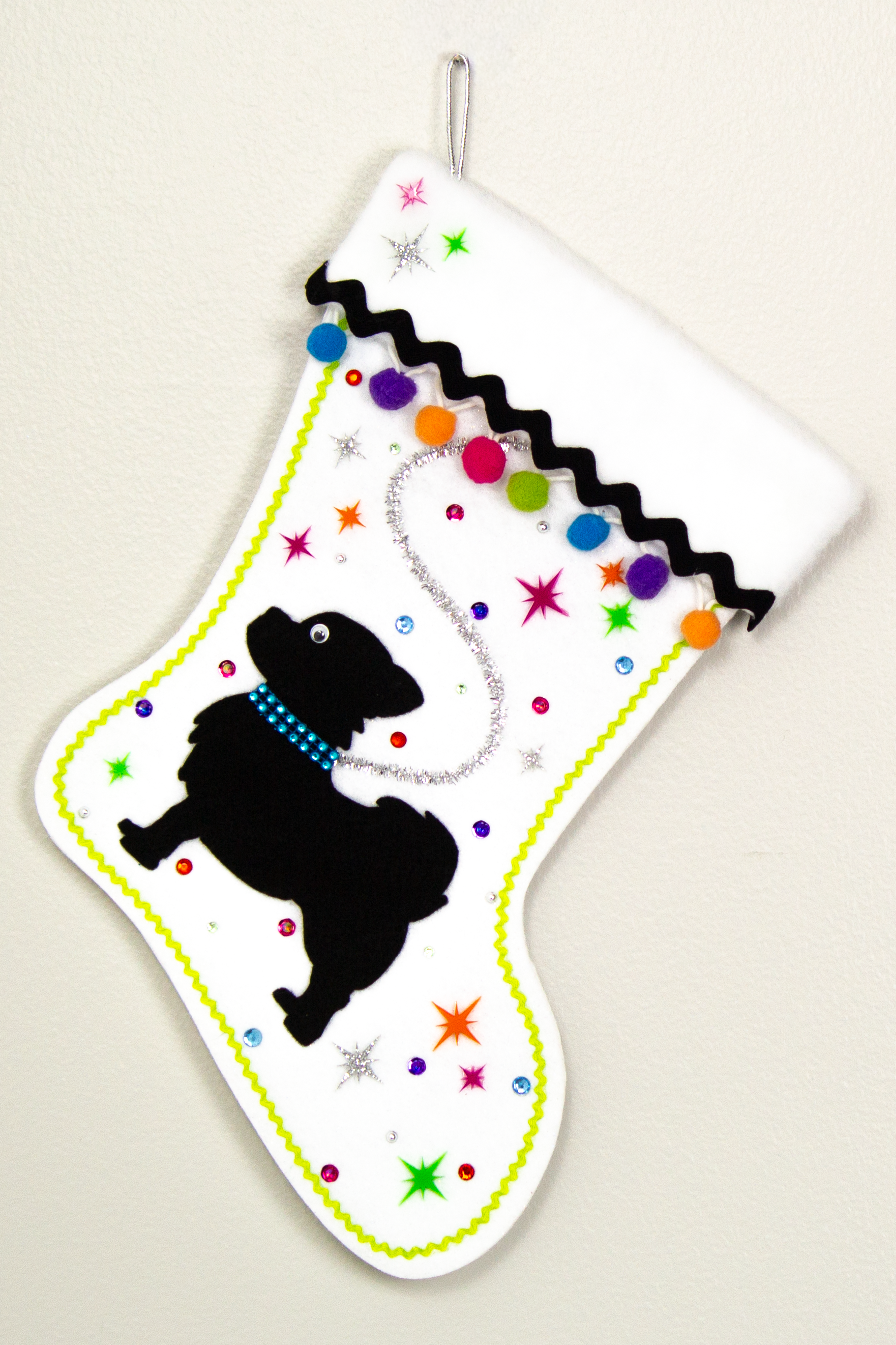 White glitter Christmas stocking with black long hair Chihuahua small dog silhouette with pom poms, starbursts and decorations in black, silver, hot pink, lime green, orange, purple and blue. (front of stocking)