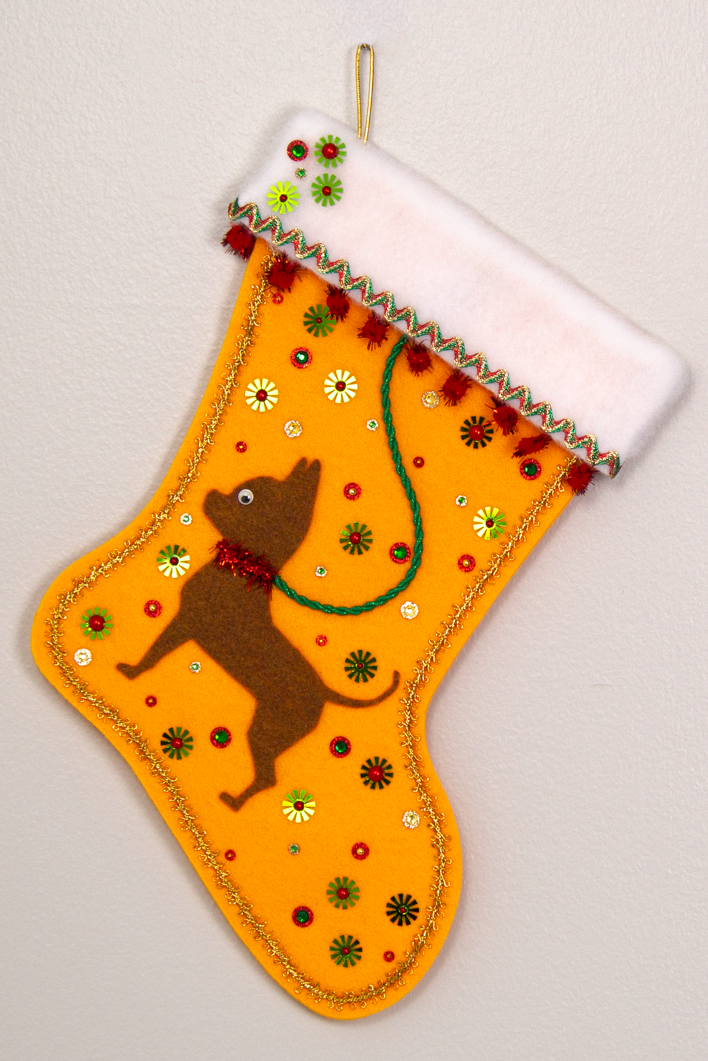 Copper short hair Chihuahua dog on Gold felt handmade Christmas stocking with sparkly pom poms, flower sequins and decorations in green, red and gold. (front of stocking)