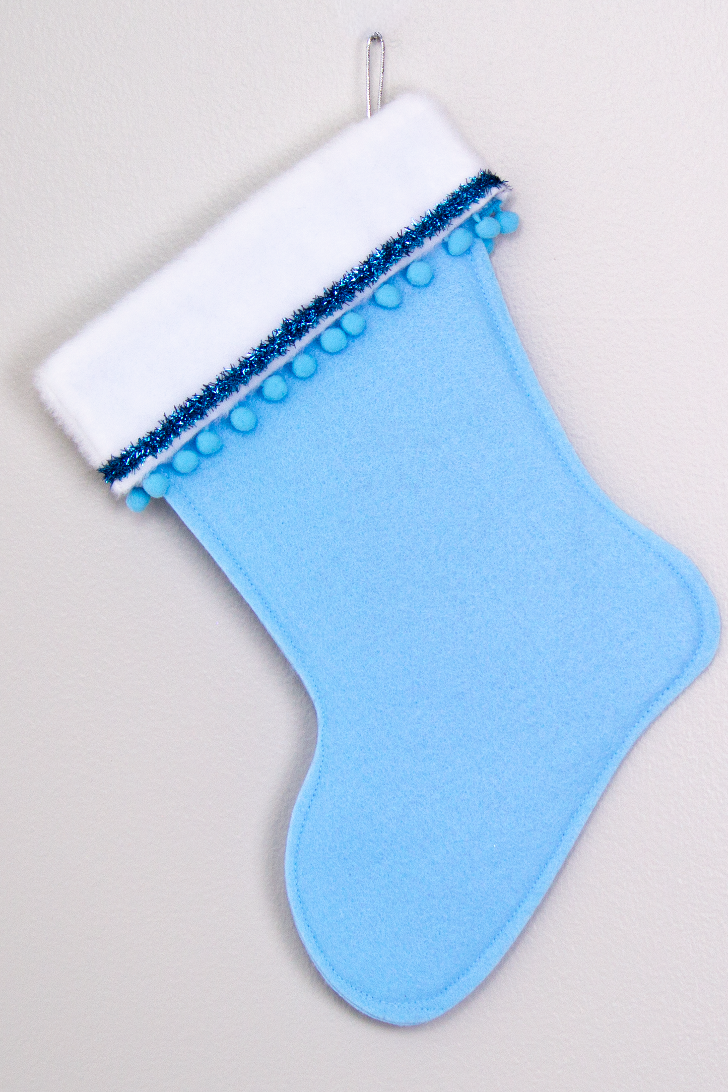 Light blue felt handmade Christmas stocking with pom poms, tinsel ribbon and decorations in blues & silver. (back of Cocktail stocking)