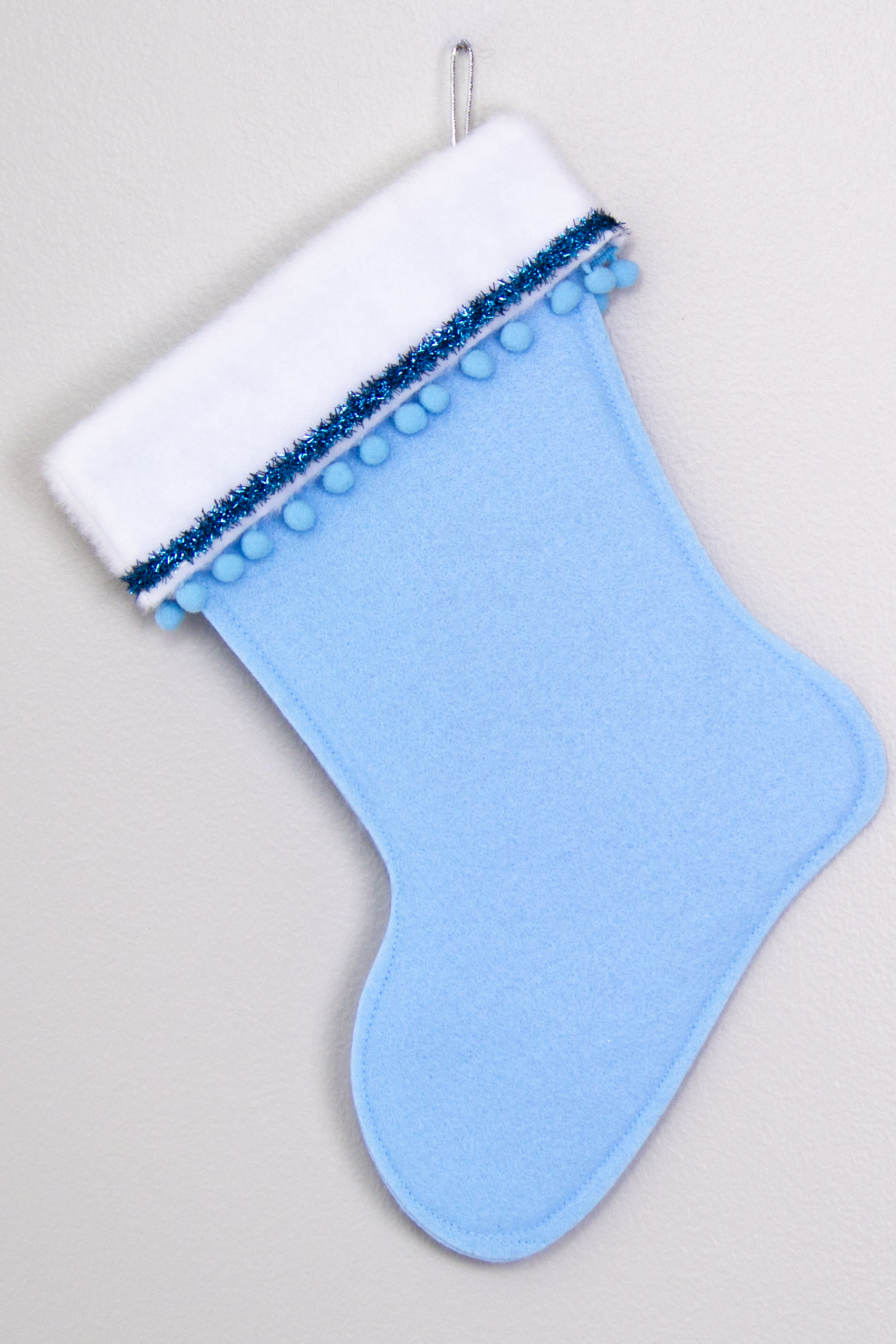 Light blue felt handmade Christmas stocking with pom poms, tinsel ribbon and decorations in blues & silver. (back of Cocktail stocking)