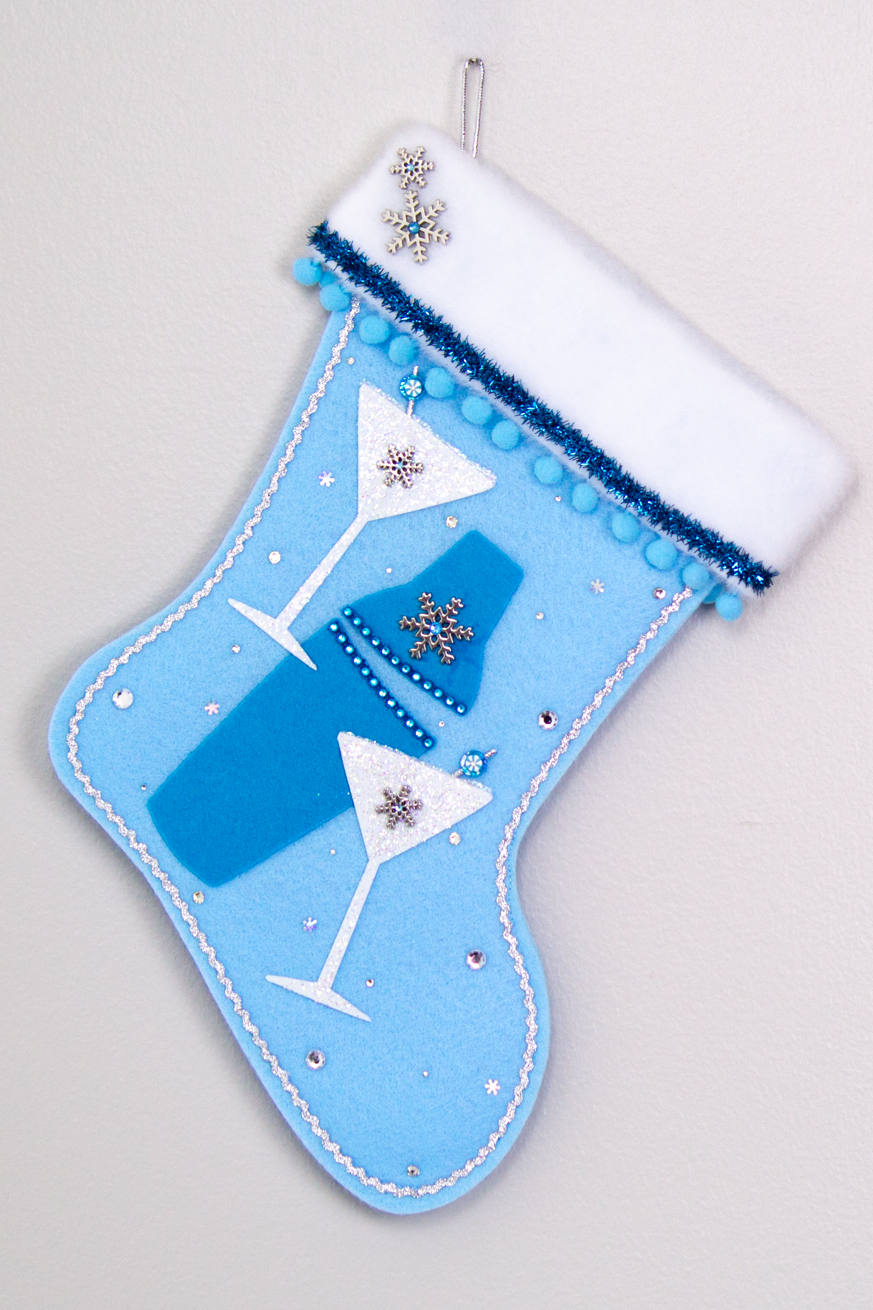 Blue felt shaker, chunky glitter painted white felt martini glasses on light blue felt handmade Christmas stocking with snowflake buttons, pom poms, tinsel ribbon and decorations in blues, white, clear & silver. (front of Cocktail stocking)