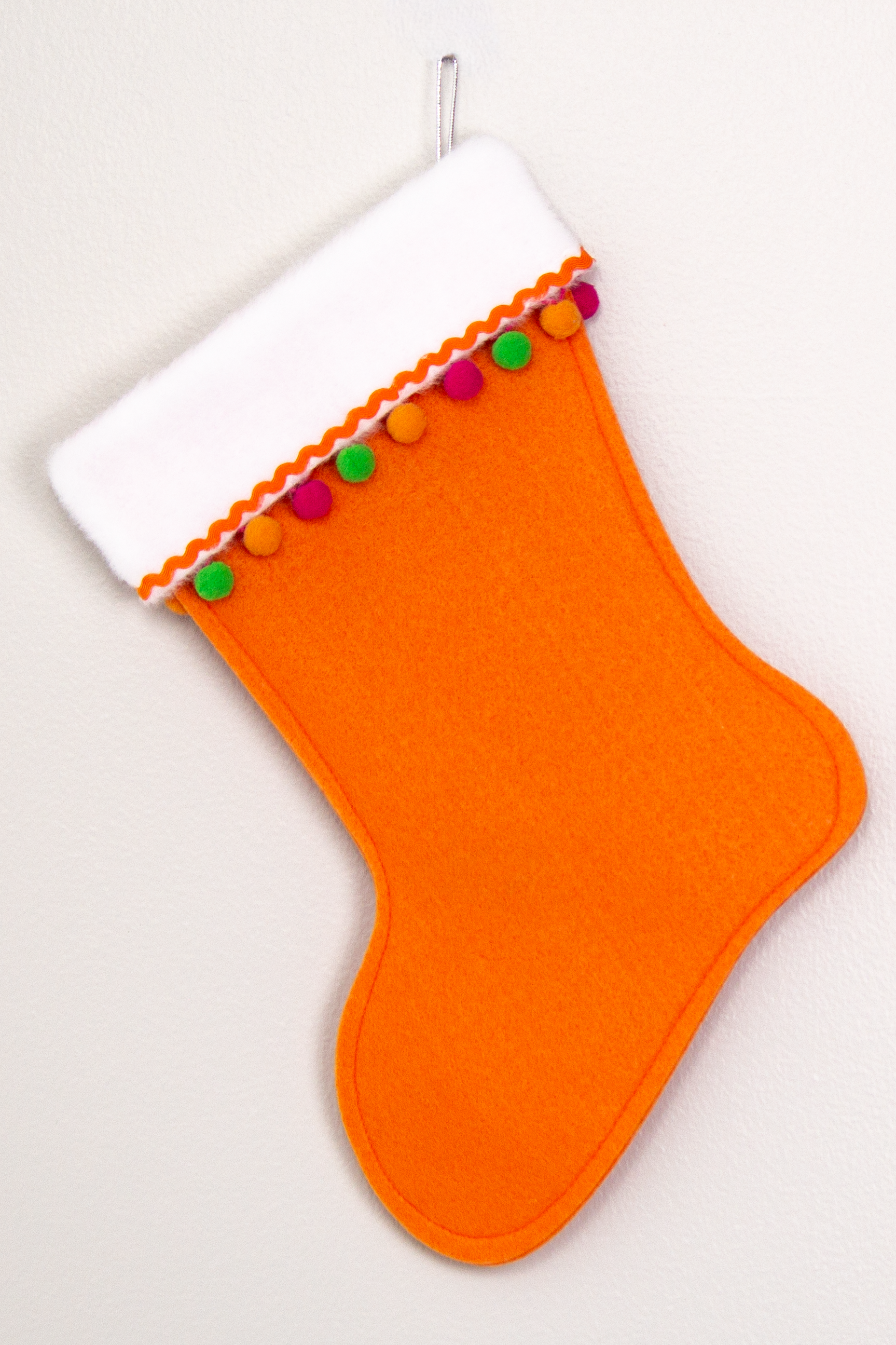 Orange felt handmade Christmas stocking with pom poms and decorated in hot pink, green, orange & silver. (back  of Cocktail stocking)