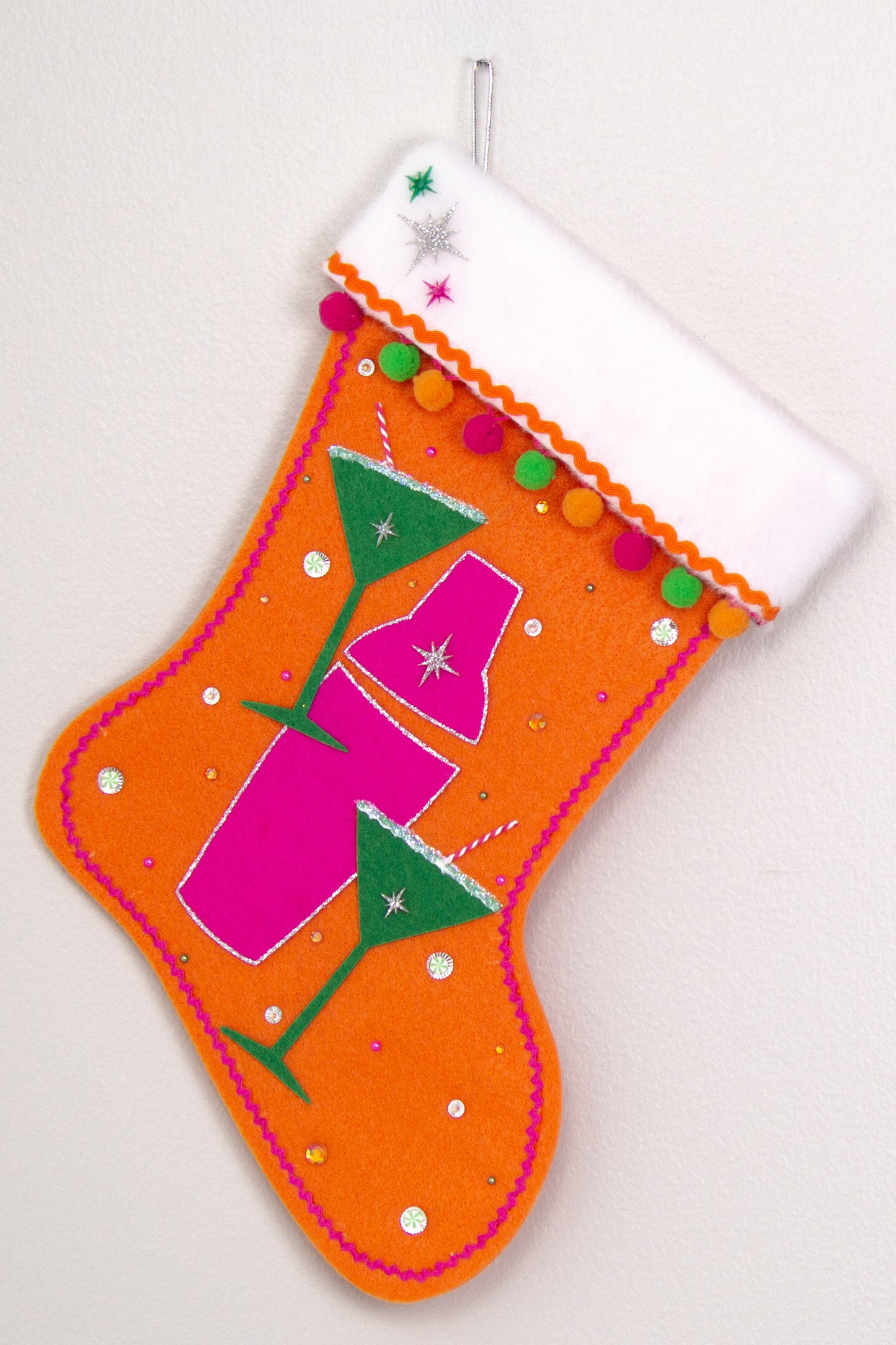 Holiday green felt martini glasses, silver glitter outlined hot pink felt shaker on orange felt handmade Christmas stocking with pom poms, acrylic starbursts and decorated in hot pink, green, orange & silver. (front of Cocktail stocking)