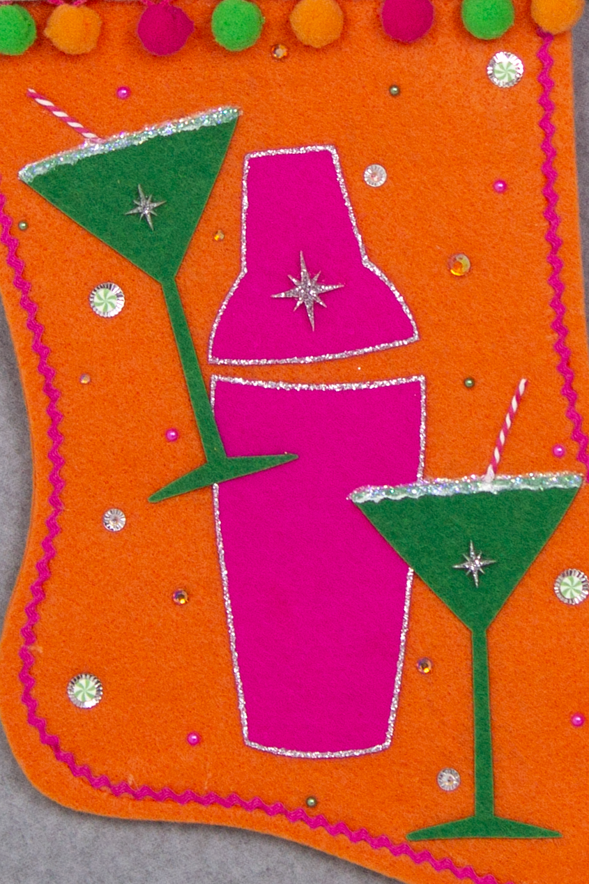 Holiday green felt martini glasses, silver glitter outlined hot pink felt shaker on orange felt handmade Christmas stocking with pom poms, acrylic starbursts and decorated in hot pink, green, orange & silver. (front of Cocktail stocking - close up detail of martini glasses and shaker)
