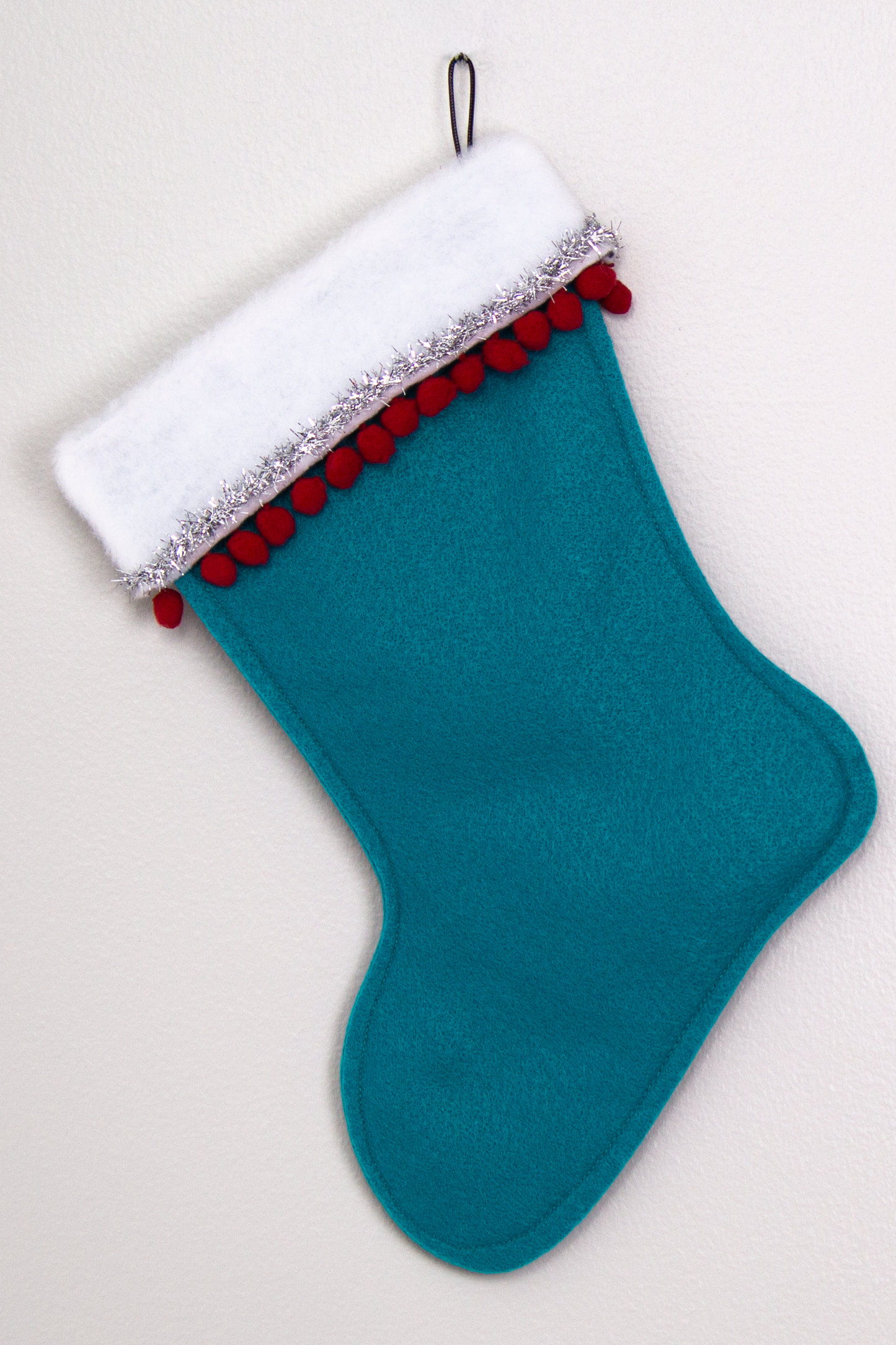 Turquoise felt handmade Christmas stocking with pom poms, tinsel ribbon and decorated in red & silver. (back of Cocktail stocking)