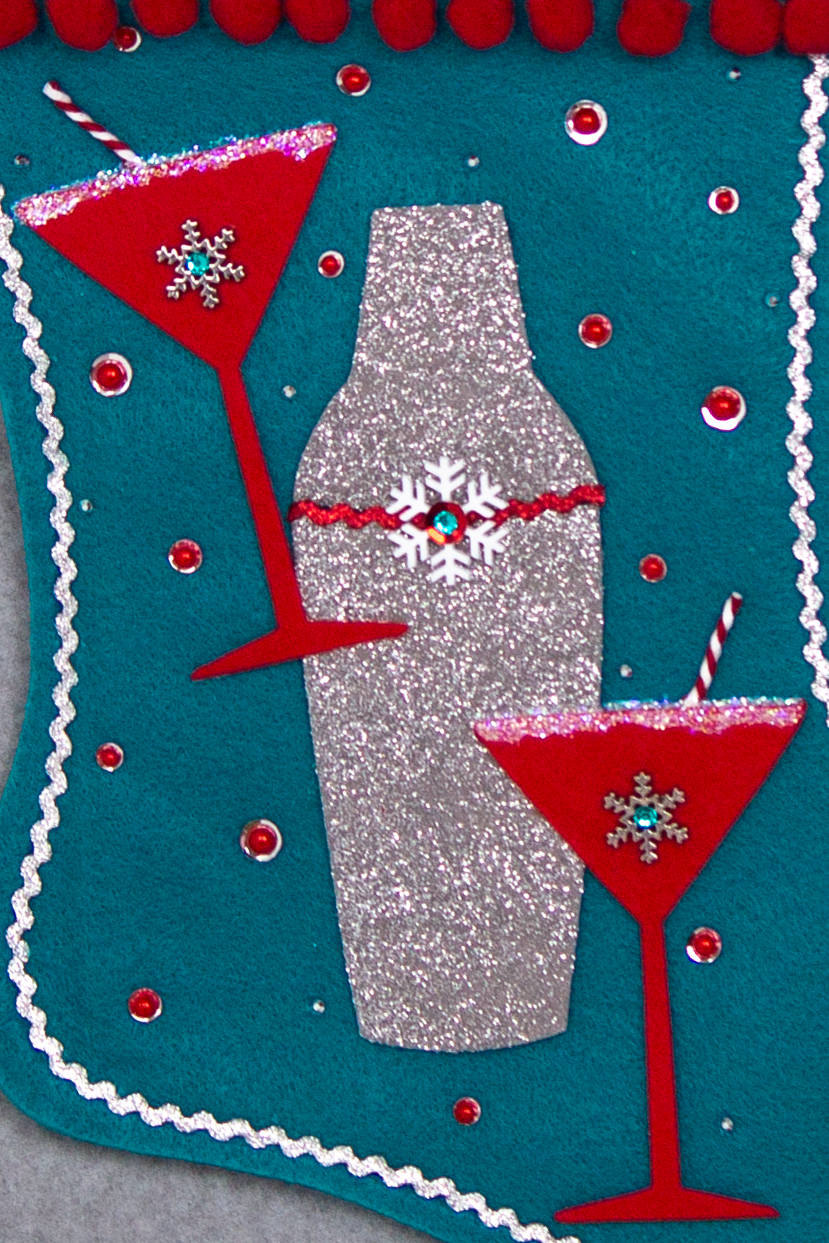 Holiday red felt martini glasses, silver glitter painted gray felt shaker on turquoise felt handmade Christmas stocking with snowflake buttons, pom poms, tinsel ribbon and decorated in  red, turquoise, white & silver.  (front of Cocktail stocking - close up detail of glasses and shaker)