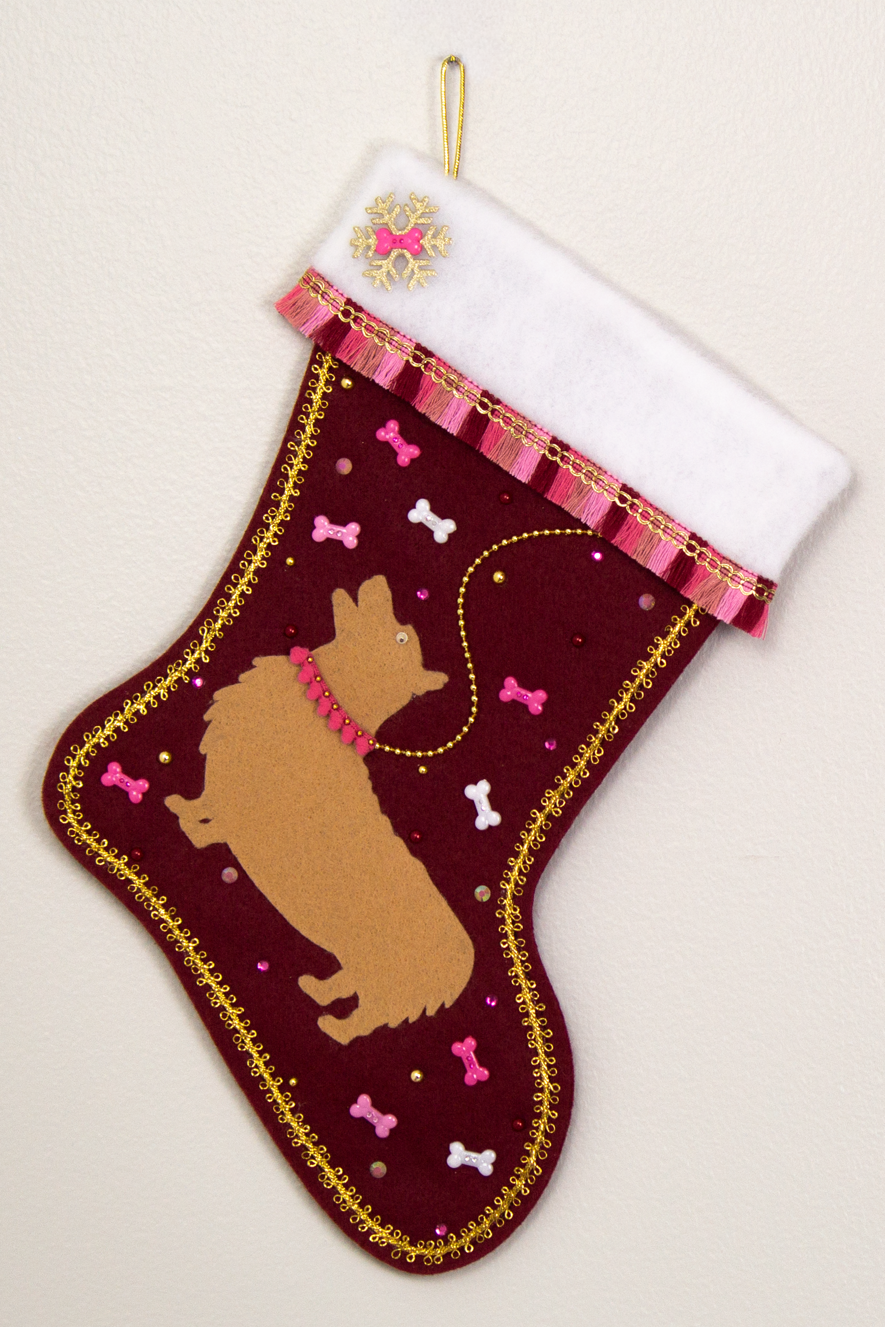 Tan Corgi dog on ruby red felt Christmas stocking with fringe, dog bones and decorations in gold, white and various pinks. (front of stocking)