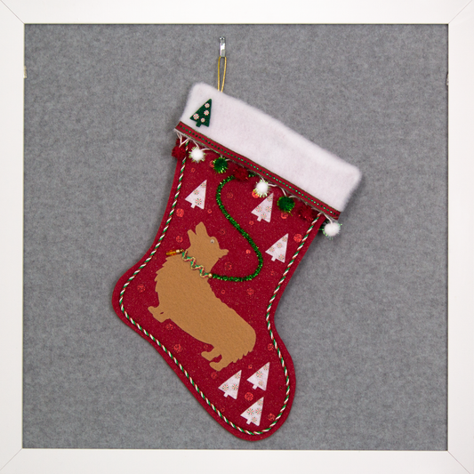 Tan Corgi on glitter red felt Christmas stocking with trees, pom poms and decorated in white, green, red and gold. (front of stocking)