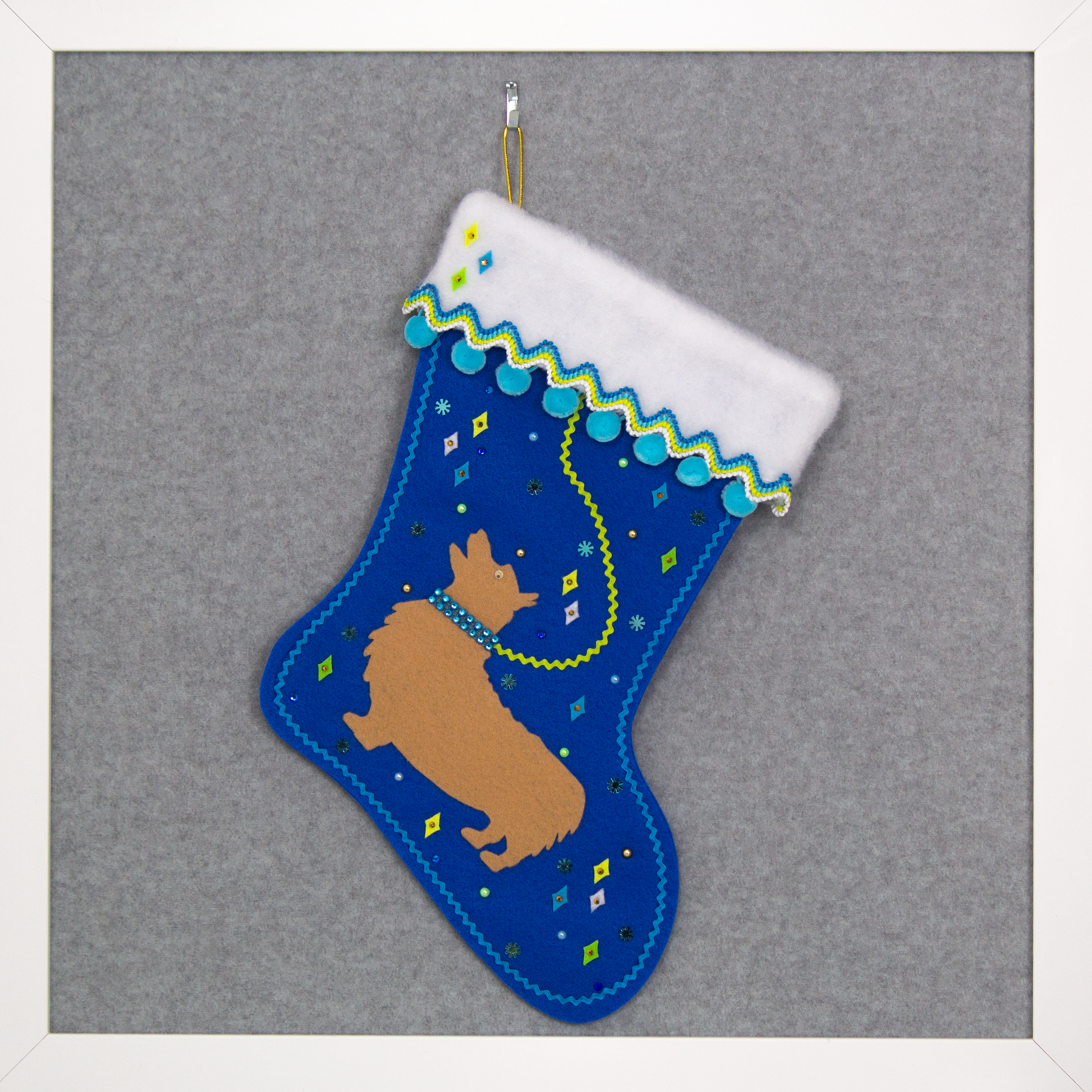 Tan Corgi dog on a royal blue felt Christmas stocking with pom poms, diamonds, snowflakes and decorated in yellow, green, blues and gold. (front of stocking)