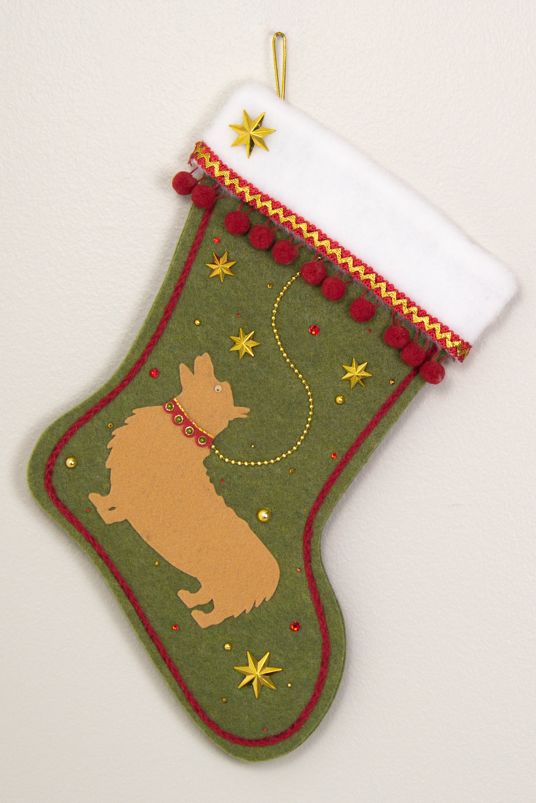 Tan Corgi dog on olive green felt Christmas stocking with stars and pom poms and decorated in gold and red. (front of stocking)