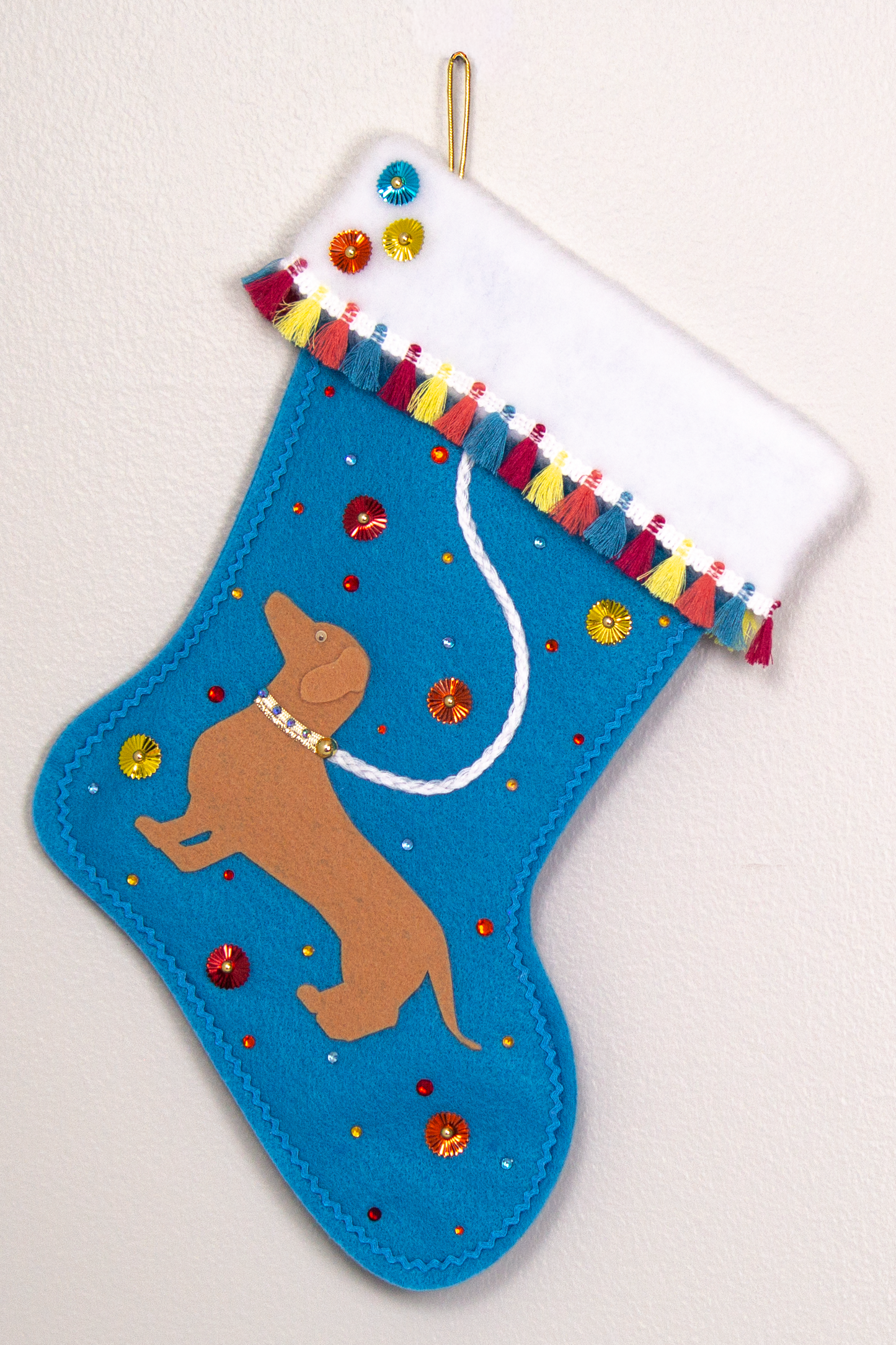 Tan Dachshund dog on peacock blue felt handmade Christmas stocking with multicolor fringe, sunburst sequins and decorated in white, blue, red, yellow, orange and gold. (front of stocking)