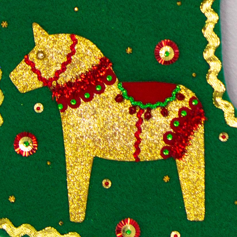 Gold glittered Dala horse on holiday green felt handmade Christmas stocking with pom poms, decorative ribbon, sunburst sequins and decorated in gold, red & green. (front of stocking - close up detail of Dala horse)