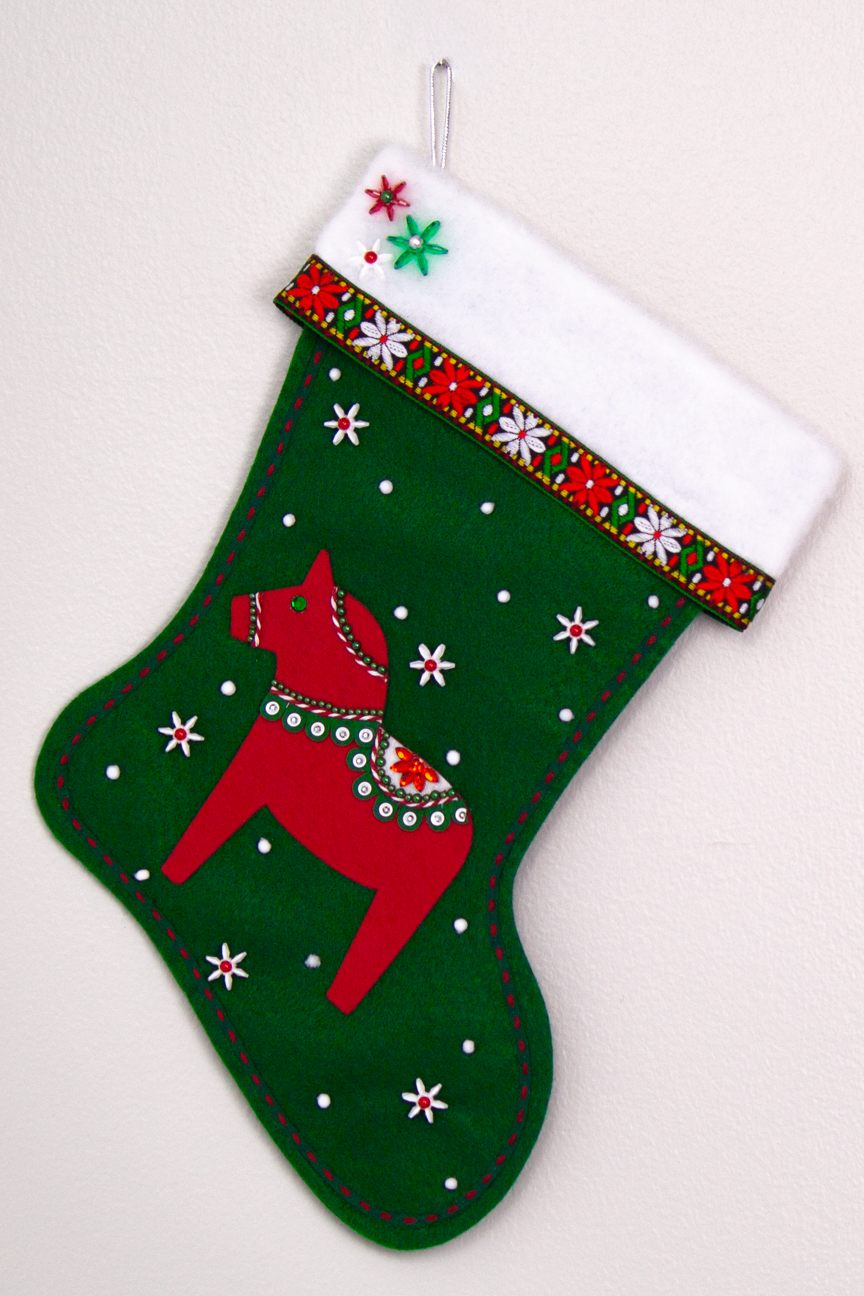 Red Dala horse on dark green felt handmade Christmas stocking with decorative ribbon, flower beads and decorated in red, green, white & silver. (front of stocking)