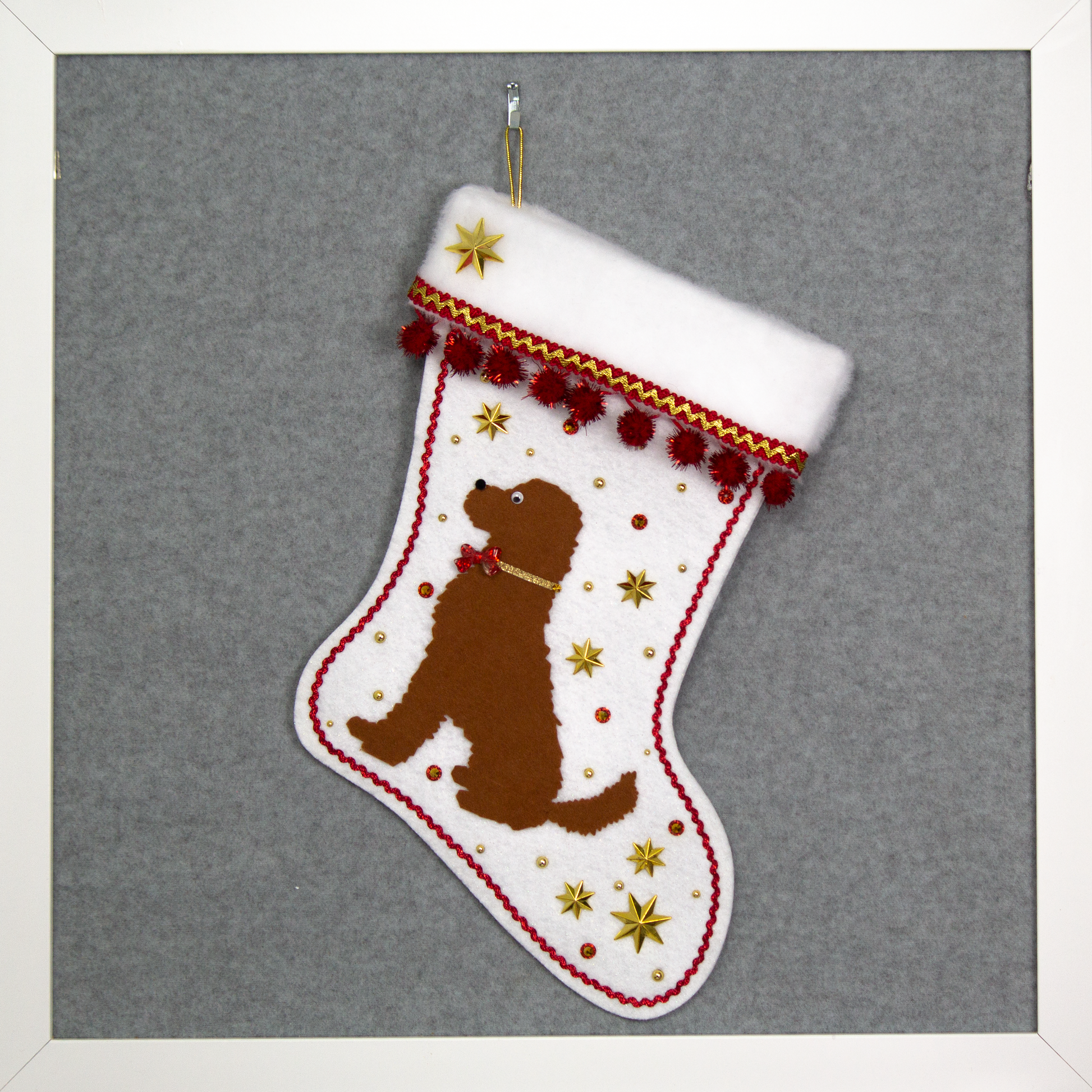 Brown labradoodle dog on a white felt Christmas stocking with red decoration.
