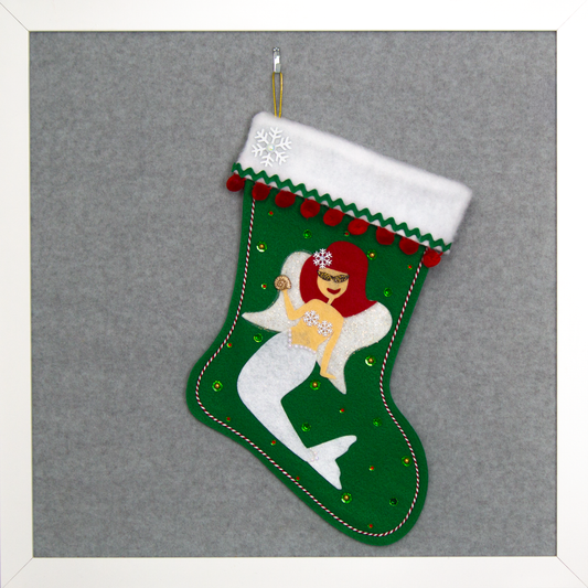 Ethel Mermaid with red hair, white glitter fin/tail, wings in white felt & gold mesh,  holding a sparkly seashell button, and a "bra" made of snowflake buttons on a holiday green felt handmade Christmas stocking decorated in white, red, green & gold. (front of stocking)