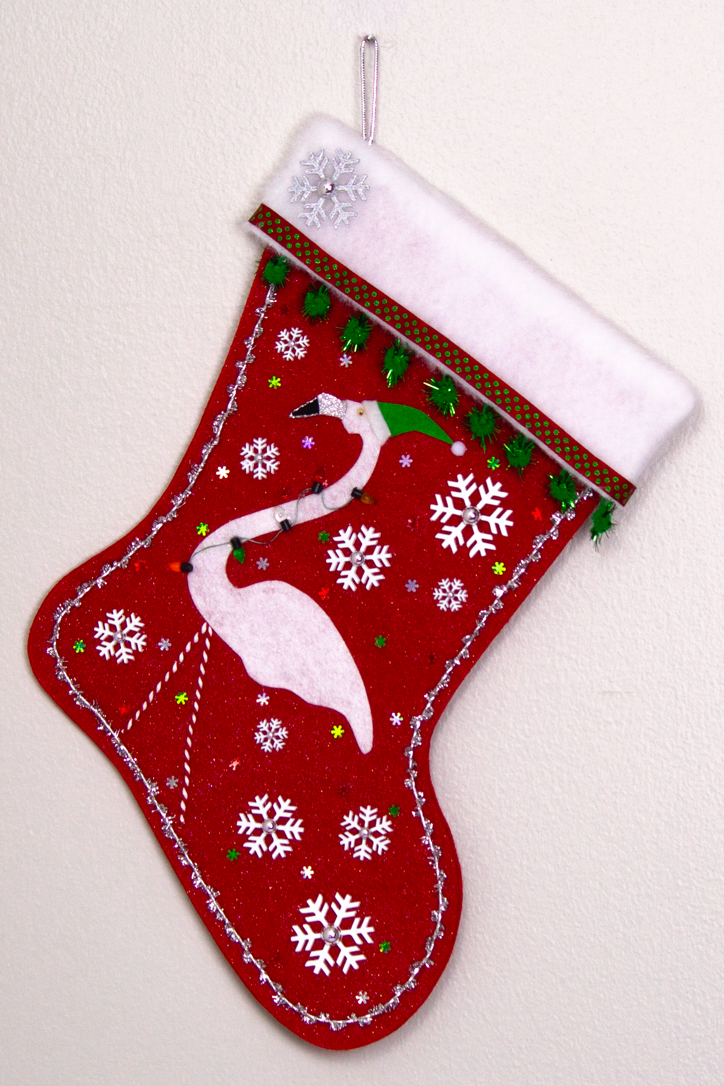 White glitter felt flamingo on red glitter felt handmade Christmas stocking with sparkly pom poms, snowflake buttons, fake lights and decorated in white, green, red & silver. (front of stocking)