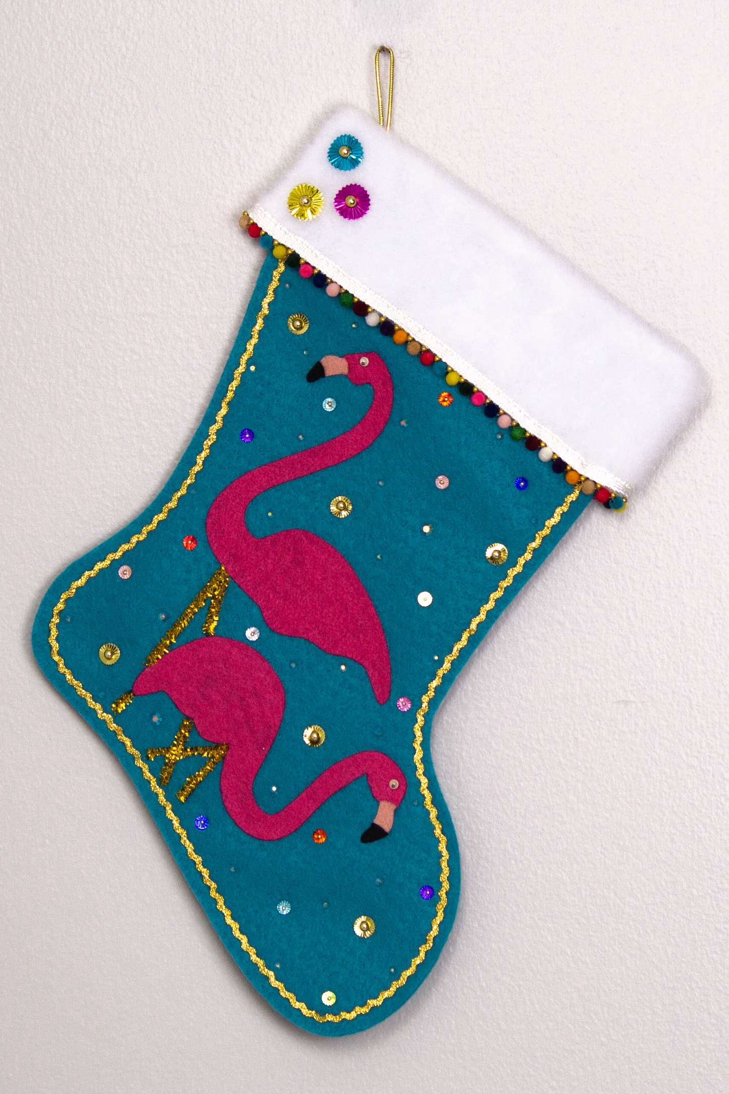 Shocking pink flamingos on turquoise felt handmade Christmas stocking with mini pom poms, sunburst sequins and decorated in gold & multicolors. (front of stocking)