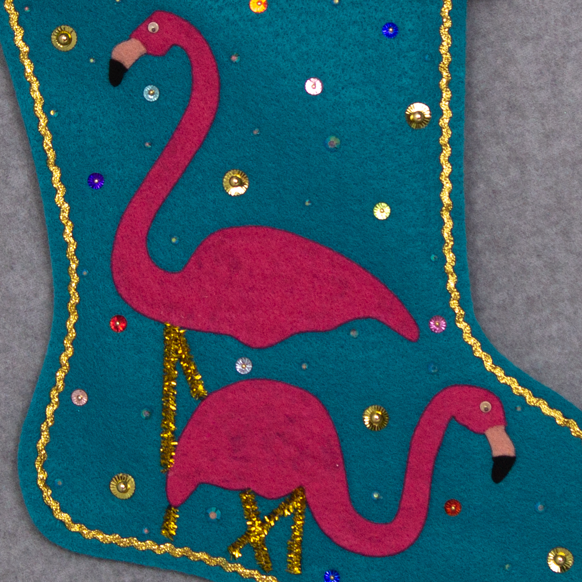 Shocking pink flamingos on turquoise felt handmade Christmas stocking with mini pom poms, sunburst sequins and decorated in gold & multicolors. (front of stocking - close up detail of flamingos)