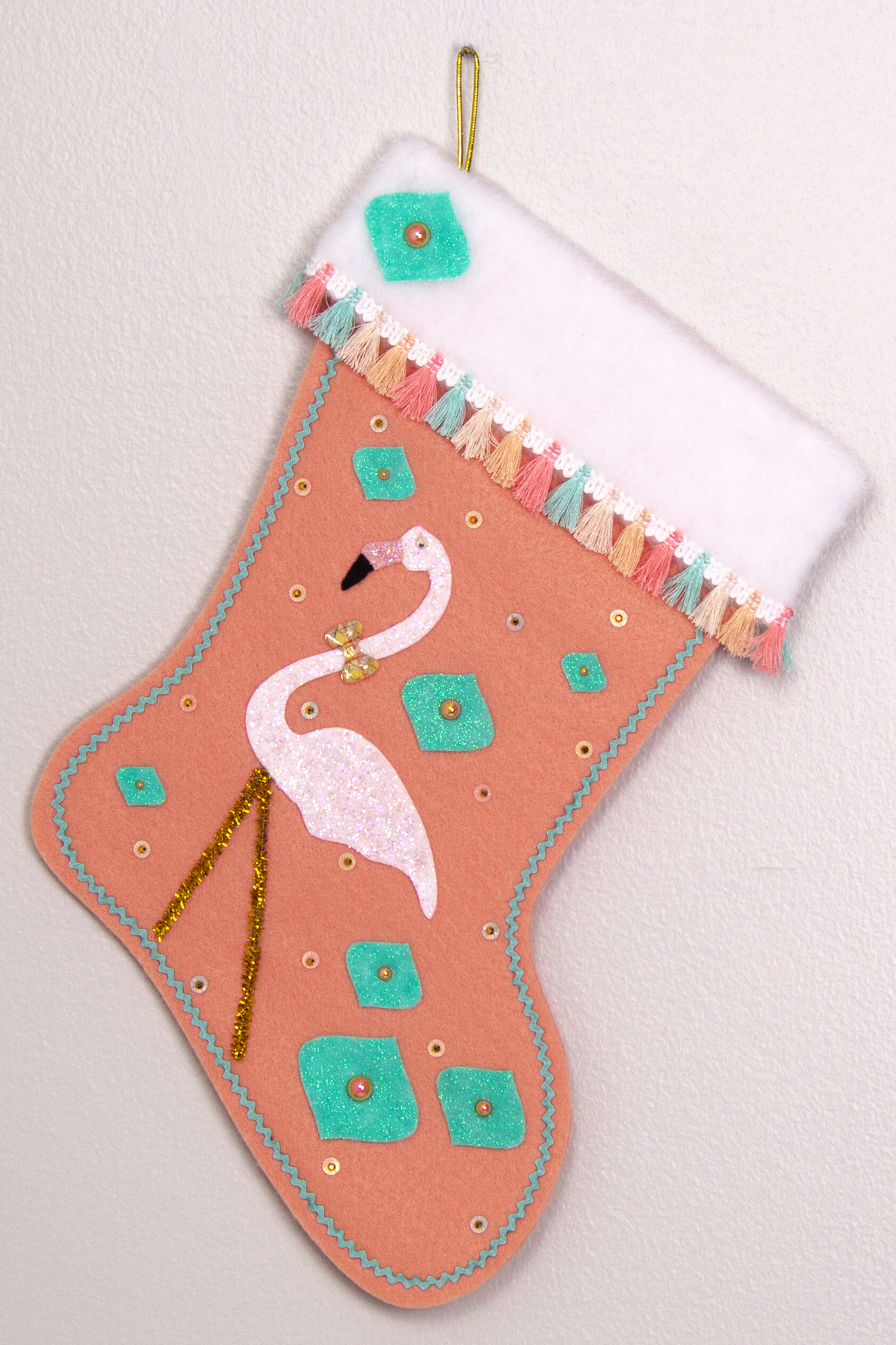 White glittery flamingo on coral felt handmade Christmas stocking with glitter painted felt onion ornament shapes, tassel fringe and decorated in coral, aqua, gold & pastel colors. (front of Flamingo stocking)