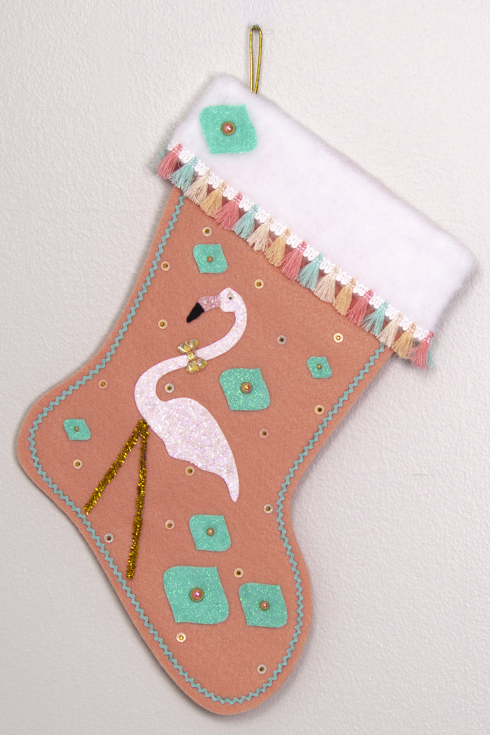 White glittery flamingo on coral felt handmade Christmas stocking with glitter painted felt onion ornament shapes, tassel fringe and decorated in coral, aqua, gold & pastel colors. (front of Flamingo stocking)