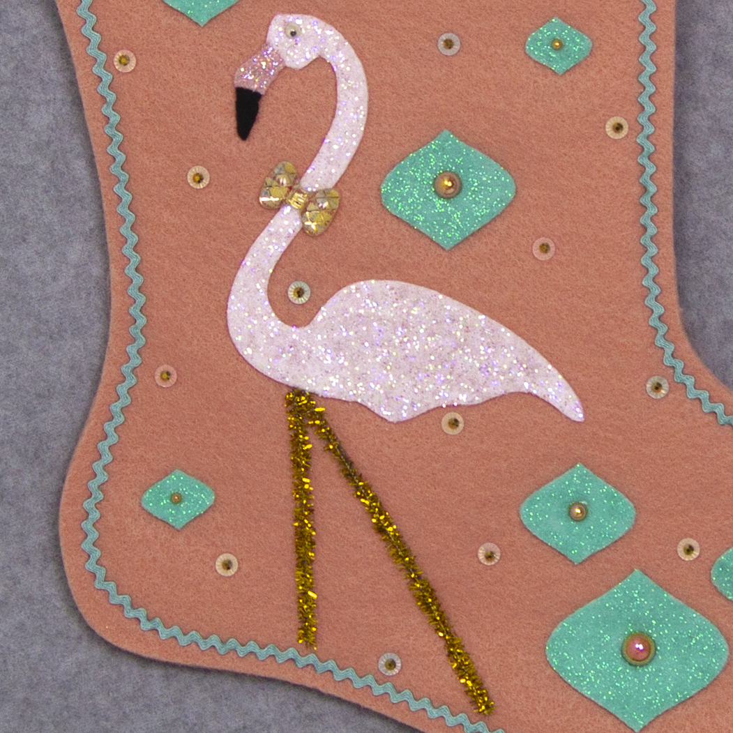 White glittery flamingo on coral felt handmade Christmas stocking with glitter painted felt onion ornament shapes, tassel fringe and decorated in coral, aqua, gold & pastel colors. (front of Flamingo stocking - close up detail of flamingo)