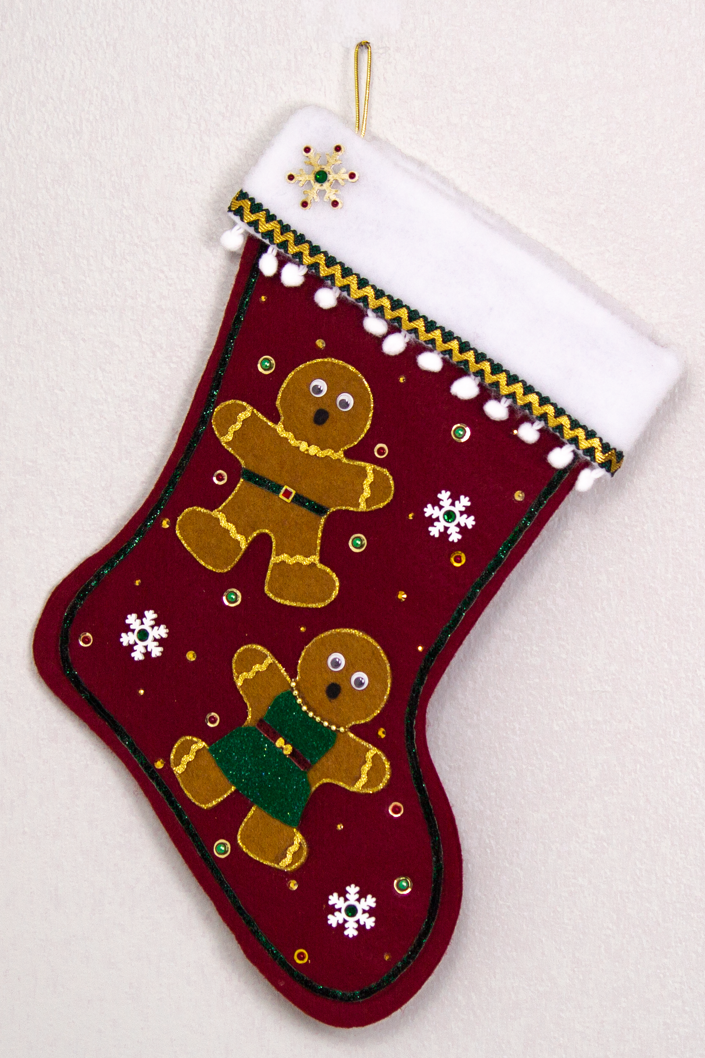 Twin copper felt Gingerbread on a ruby red felt handmade Christmas stocking with pom poms, wood snowflakes and decorated in white, green, red & gold. (front of stocking)
