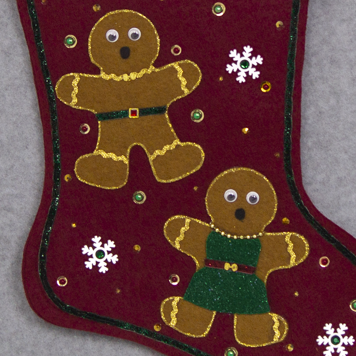 Twin copper felt Gingerbread on a ruby red felt handmade Christmas stocking with pom poms, wood snowflakes and decorated in white, green, red & gold. (front of stocking - close up detail of Gingerbread people)