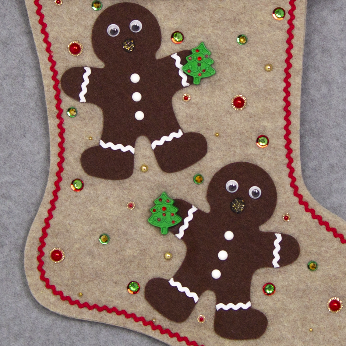 Twin dark brown Gingerbread men on sandstone beige felt handmade Christmas stocking with brown fur trim, decorative ribbon, tree buttons, a wreath button and decorated in red, green, white & gold. (front of stocking - close up detail of Gingerbread men)